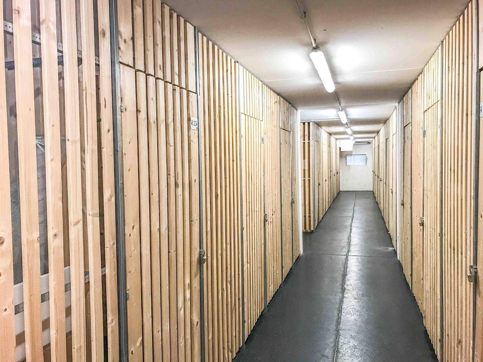 Langer Flur mit individuellen Lagerabteilen aus Holzlatten für zusätzlichen Stauraum im Keller.