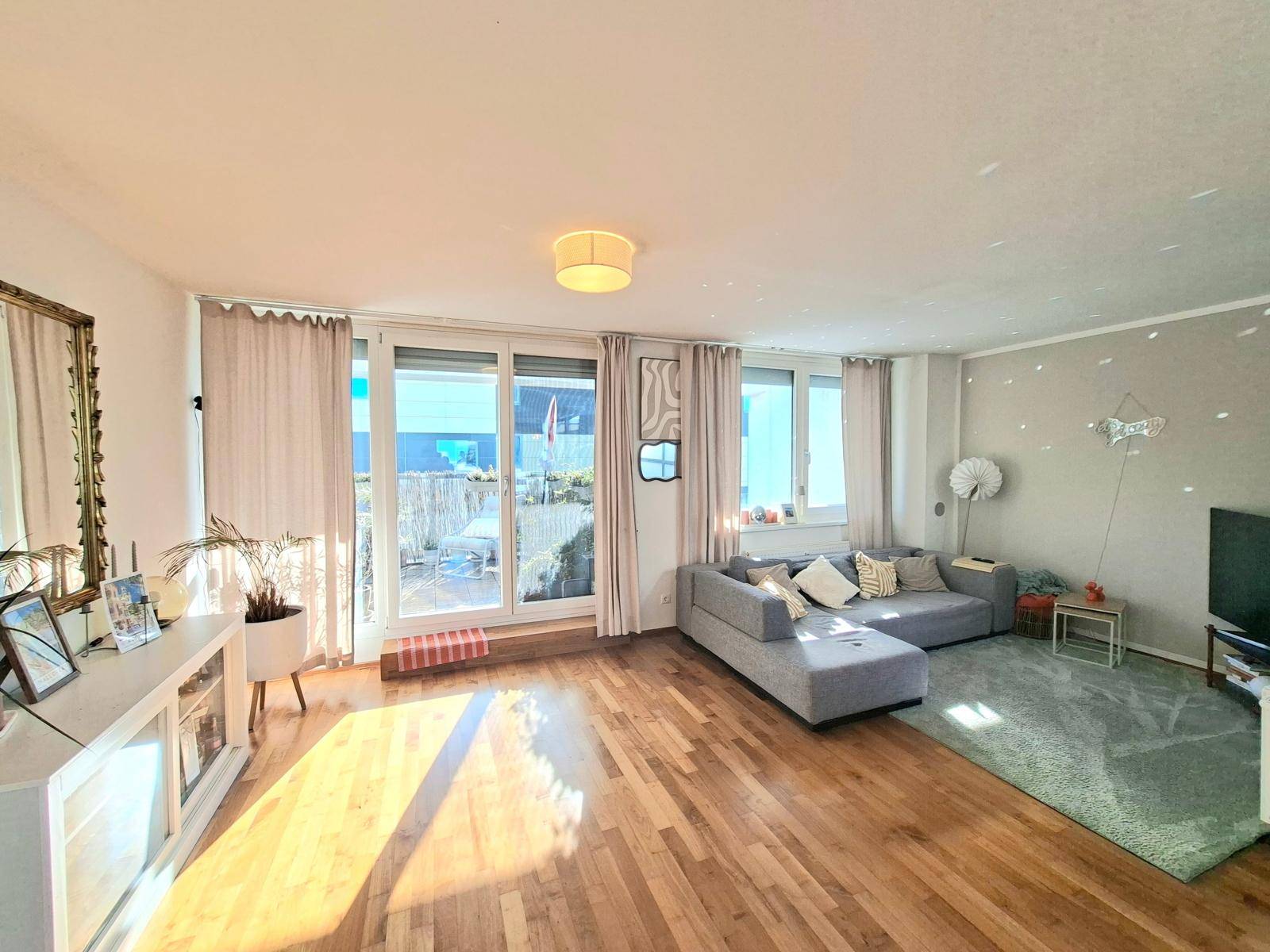 Geräumiges Wohnzimmer mit bequemer Couch, Holzboden und Zugang zu einem Außenbereich.
