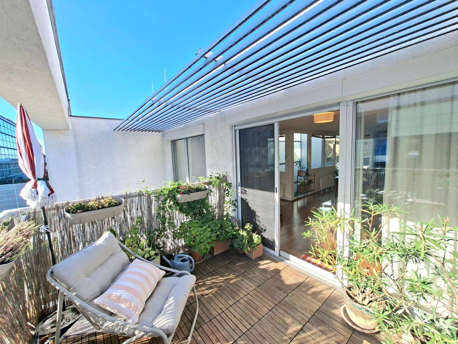 Heller Balkon mit Holzboden, Pflanzen und Blick auf die Stadt, verbunden mit dem Innenbereich.