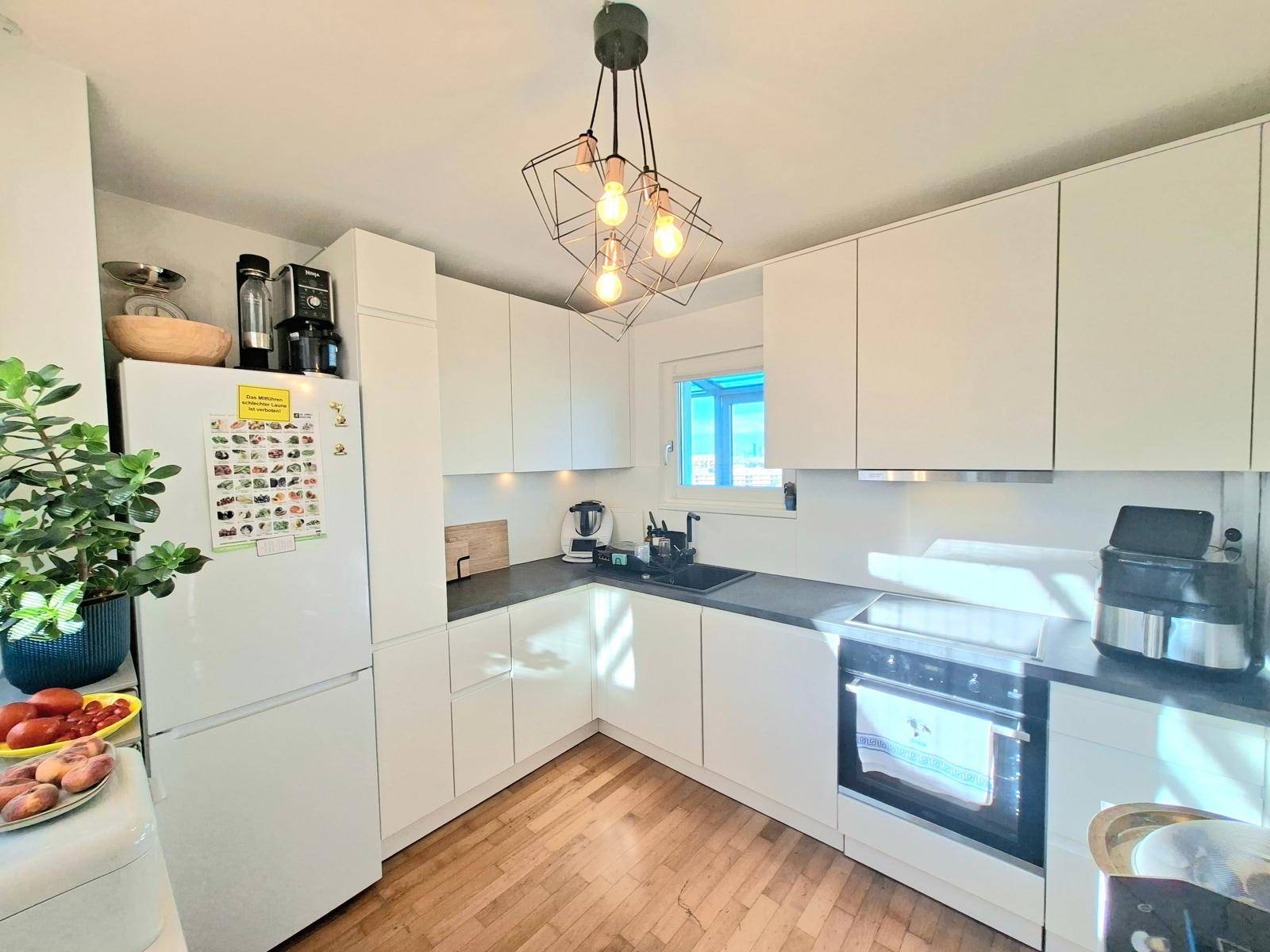 Moderne Küche mit weißen Schränken, dunkler Arbeitsplatte und integriertem Backofen.
