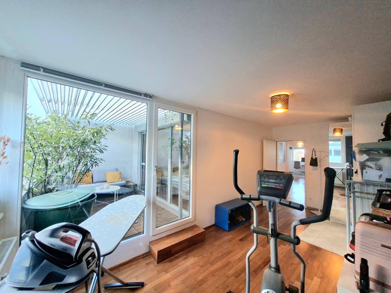 Innenraum mit Fitnessgeräten und direktem Zugang zu einer möblierten Terrasse mit Whirlpool.