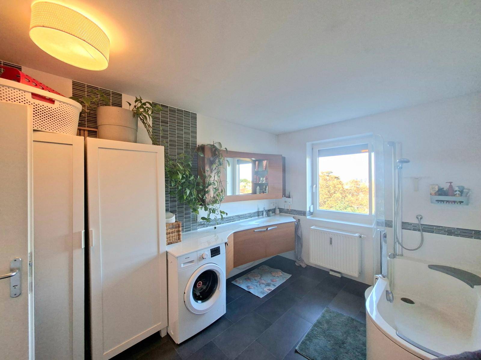 Geräumiges Badezimmer mit Waschmaschine, Waschtisch und einer Eckbadewanne mit Duschfunktion.