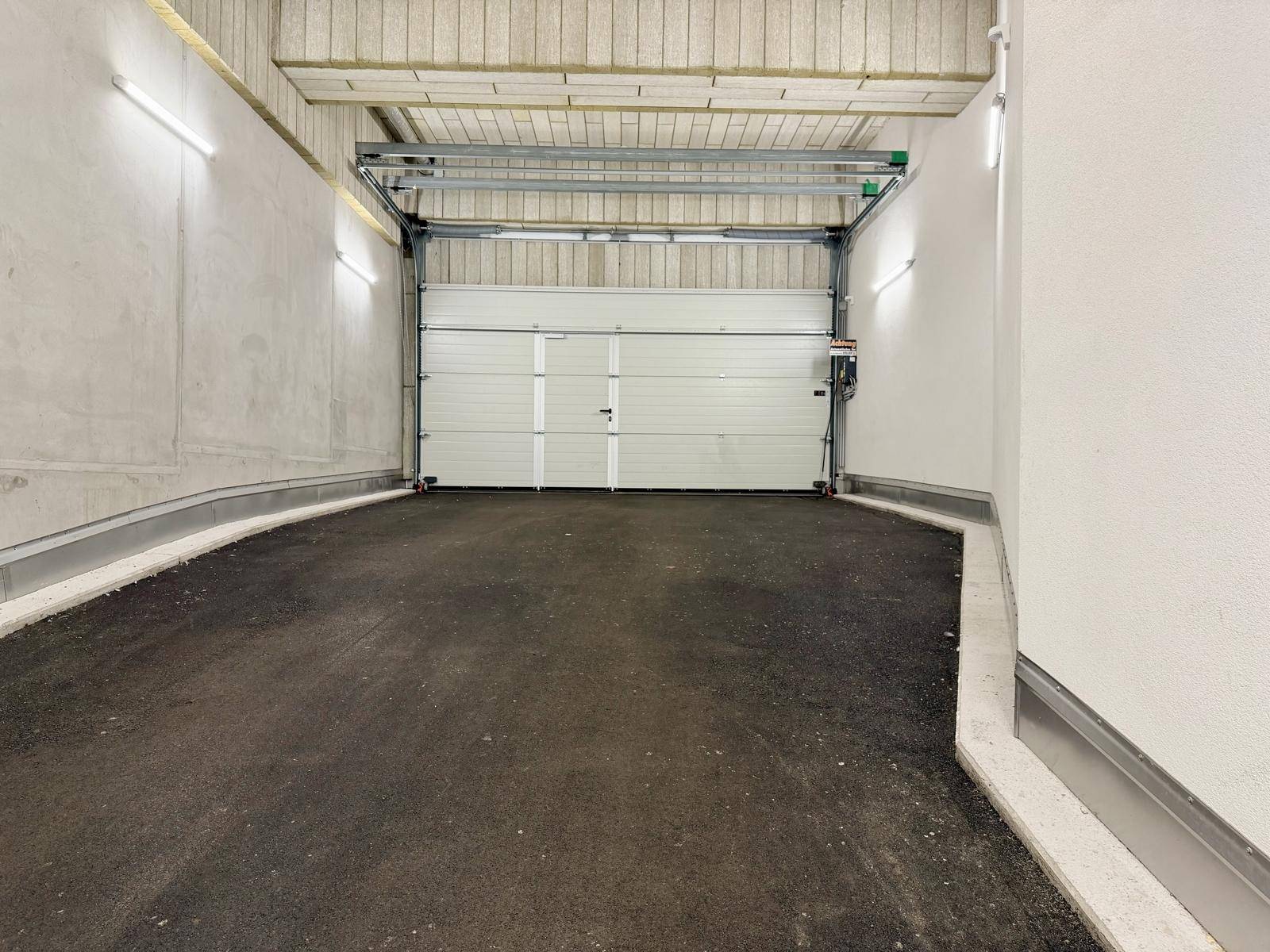 Ausfahrtbereich einer Tiefgarage mit automatischem Rolltor und heller Beleuchtung an den Wänden.