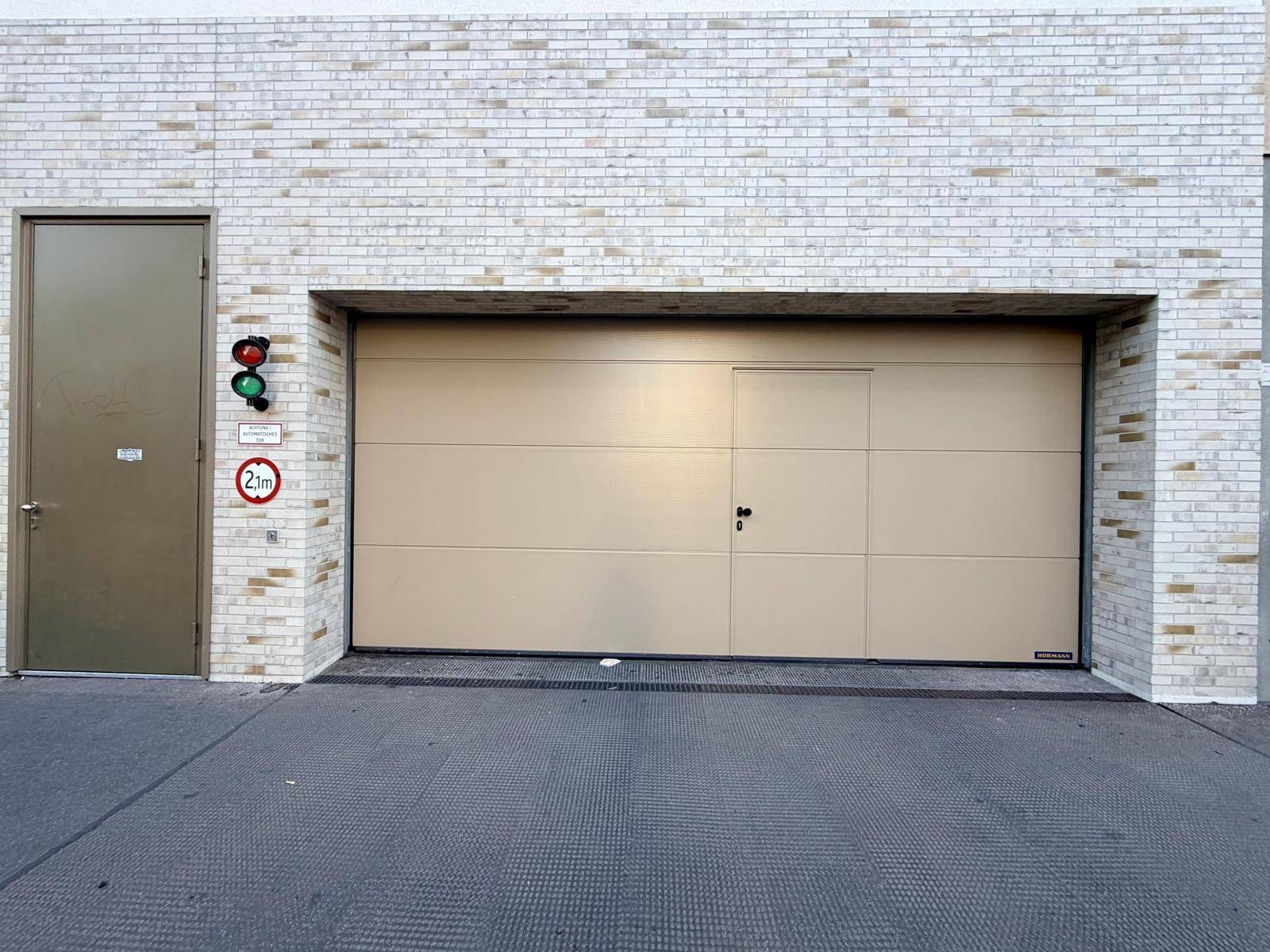 Geschlossenes Garagentor einer Tiefgarage mit integrierter Tür und heller Ziegelmauer.