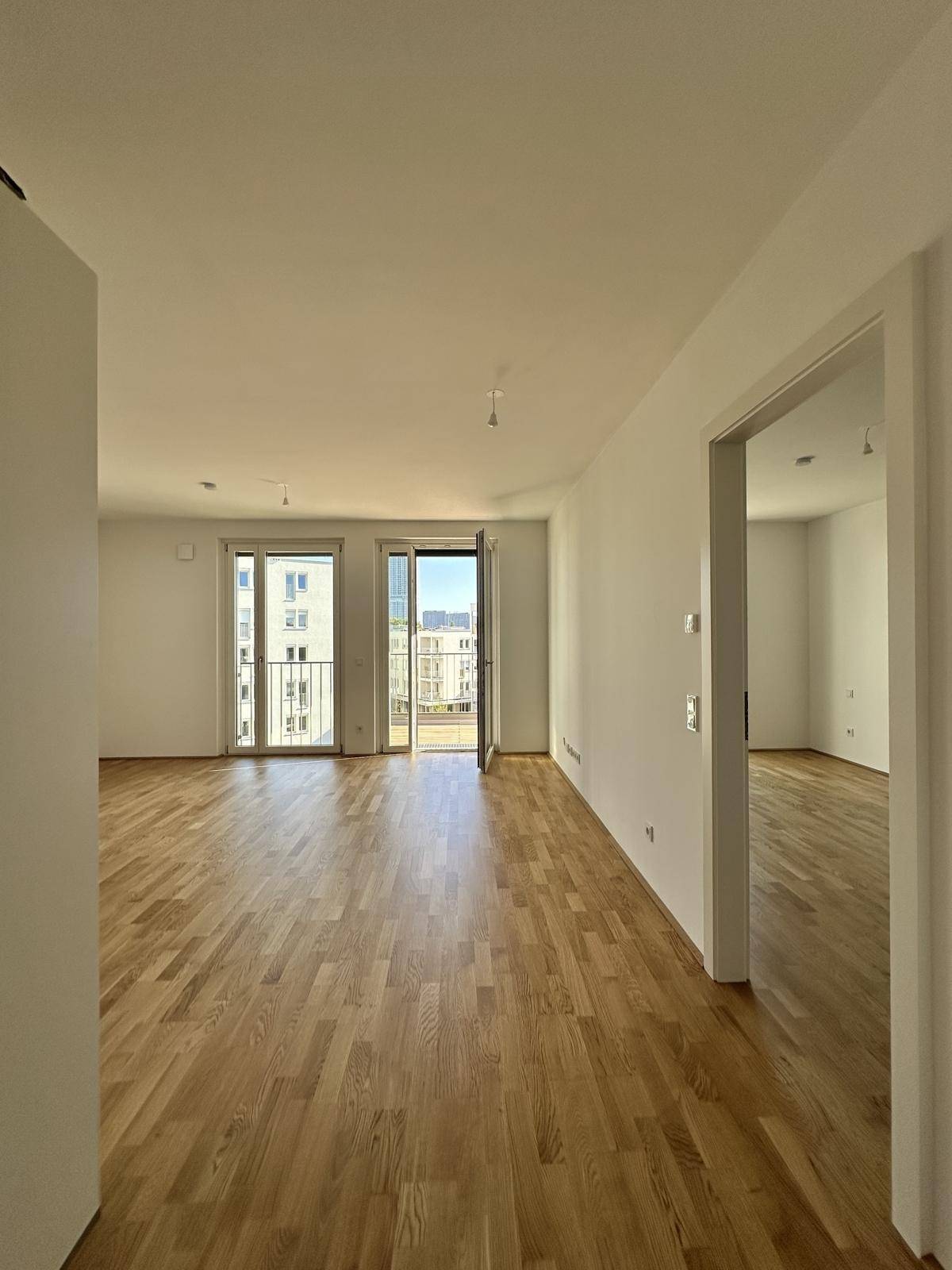 Helles Wohnzimmer mit Parkettboden und Zugang zu einem sonnigen Balkon, viel Tageslicht.