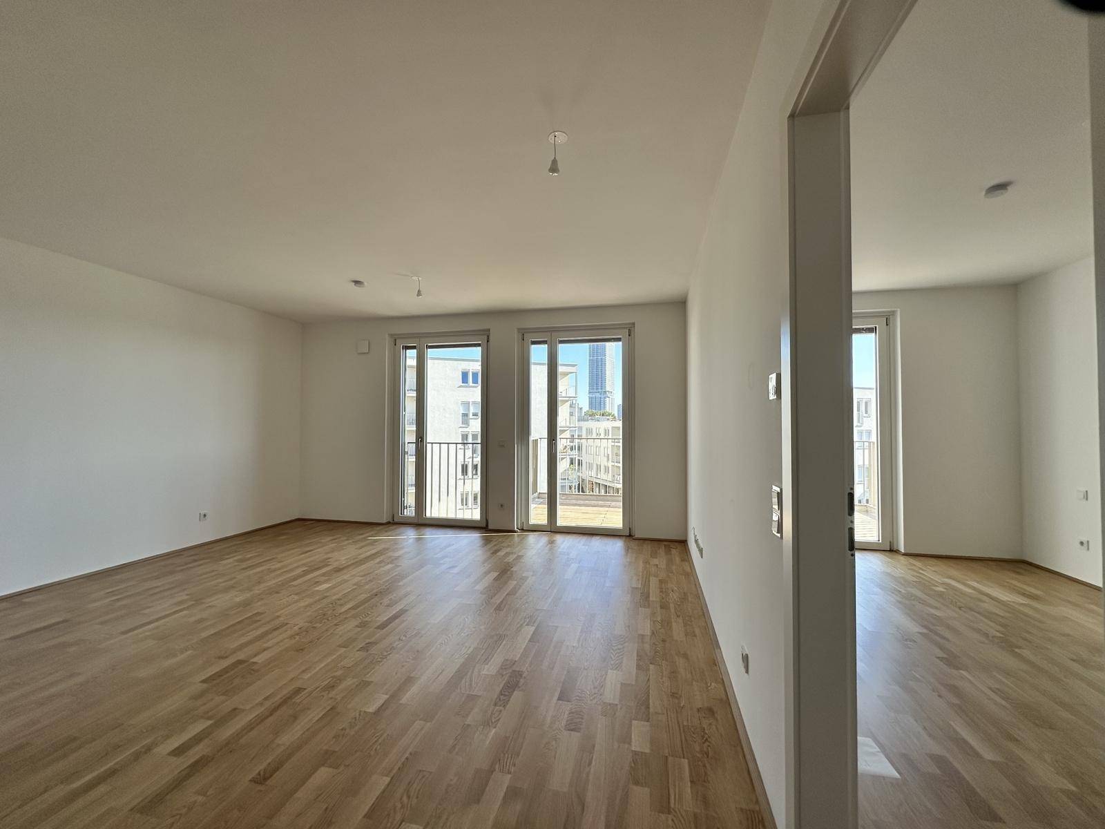 Geräumiges Wohnzimmer mit Parkettboden und zwei Balkonzugängen, sehr hell und offen.