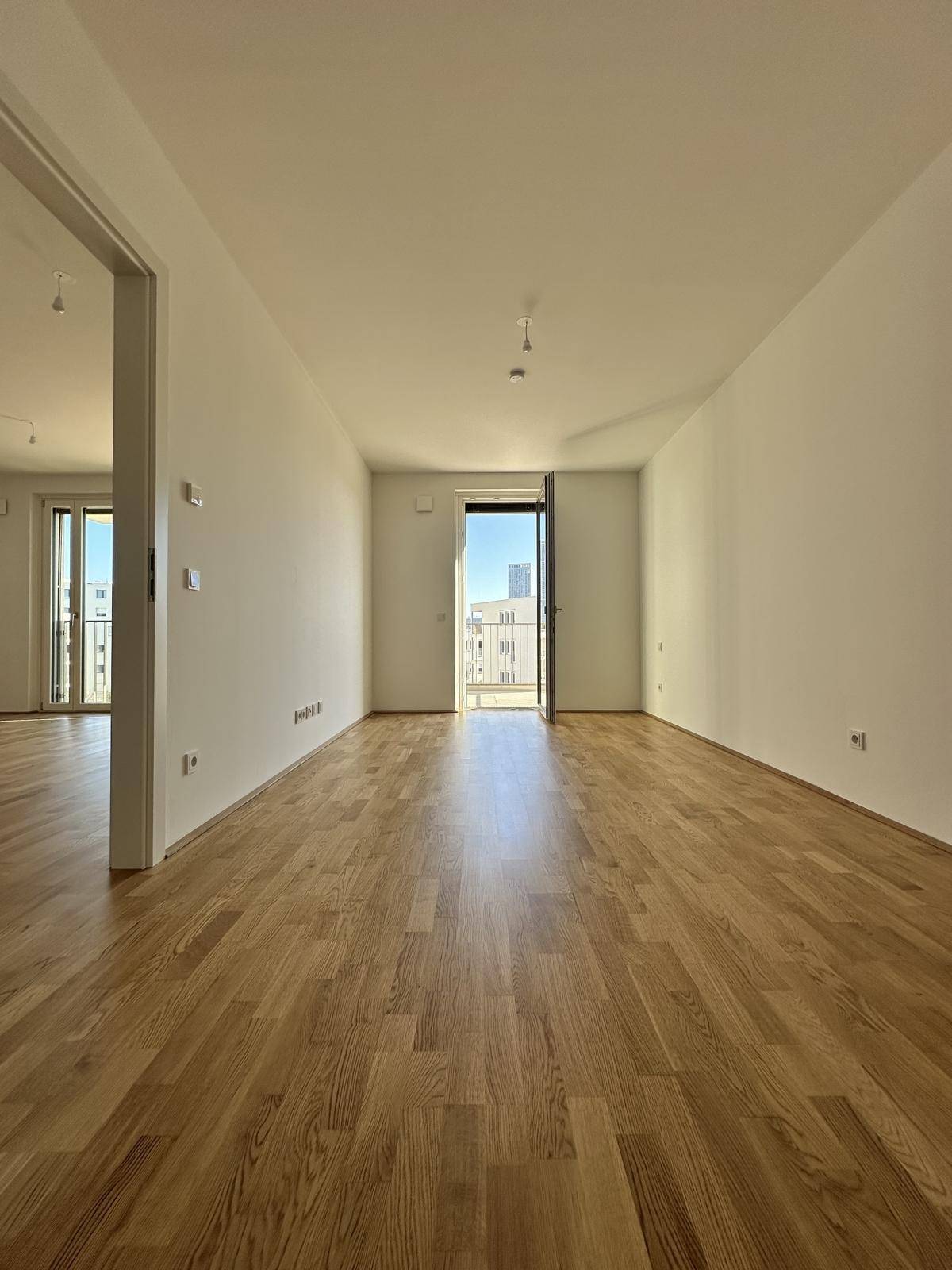 Helles Wohnzimmer mit Parkettboden und Balkonzugang, bereit für individuelle Gestaltung.