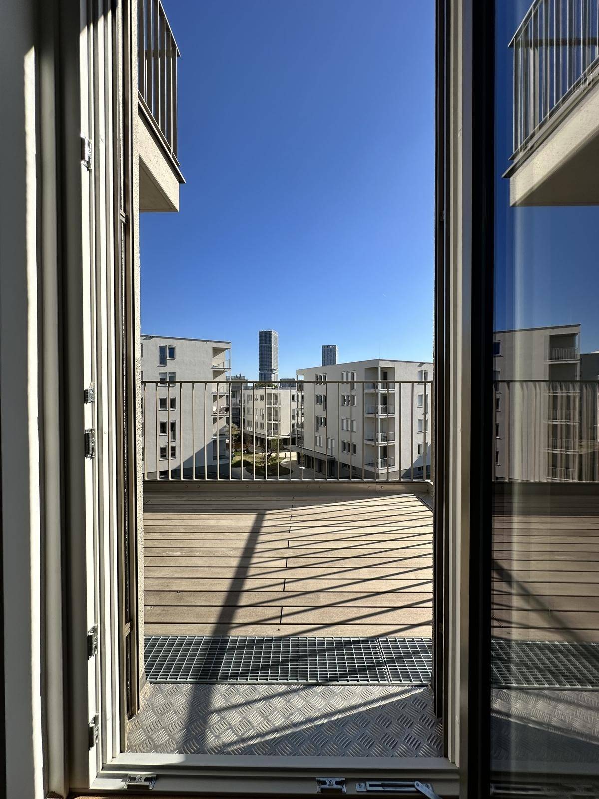 Blick vom Balkon auf die umliegenden Neubauten und die Stadt, mit weitem Horizont.
