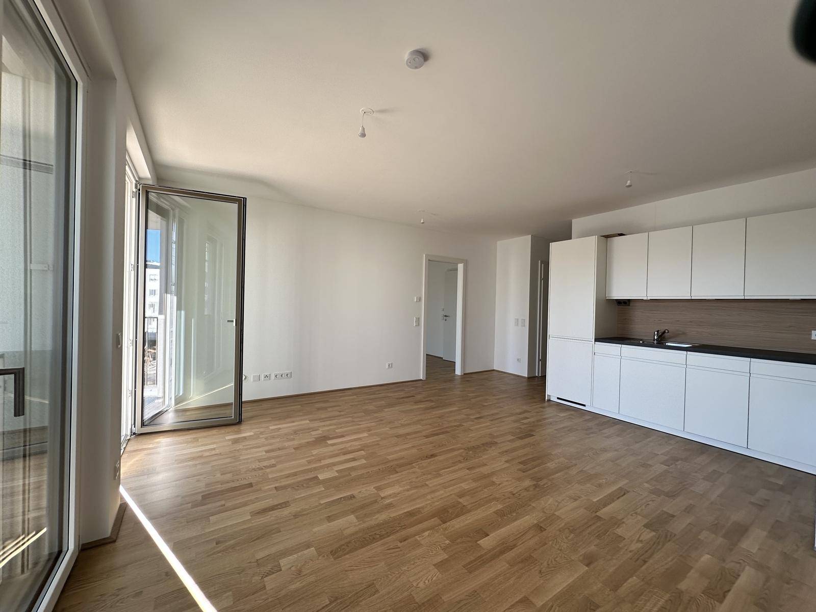 Lichtdurchfluteter Wohnbereich mit offener Küche und Zugang zum Balkon, ideal für modernes Wohnen.