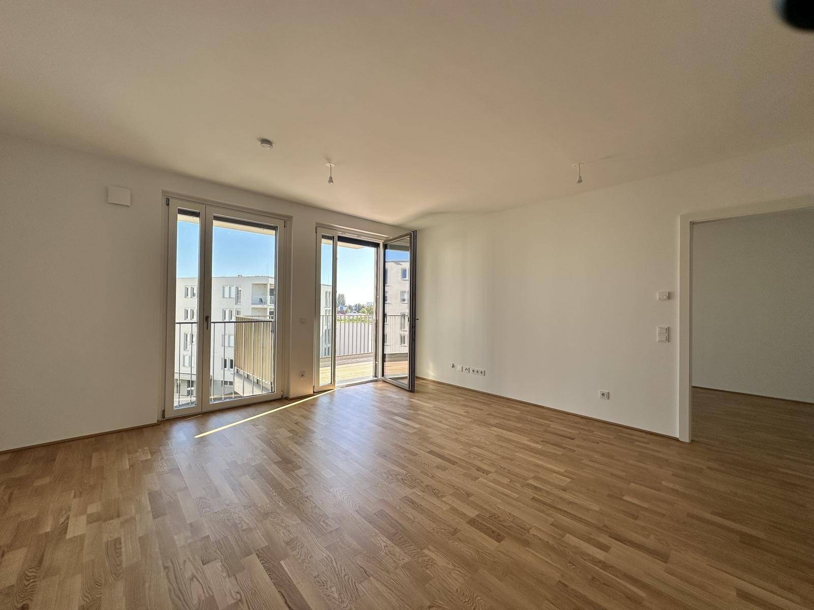 Geräumiges Wohnzimmer mit Parkettboden und Zugang zu einem sonnigen Balkon, lichtdurchflutet.