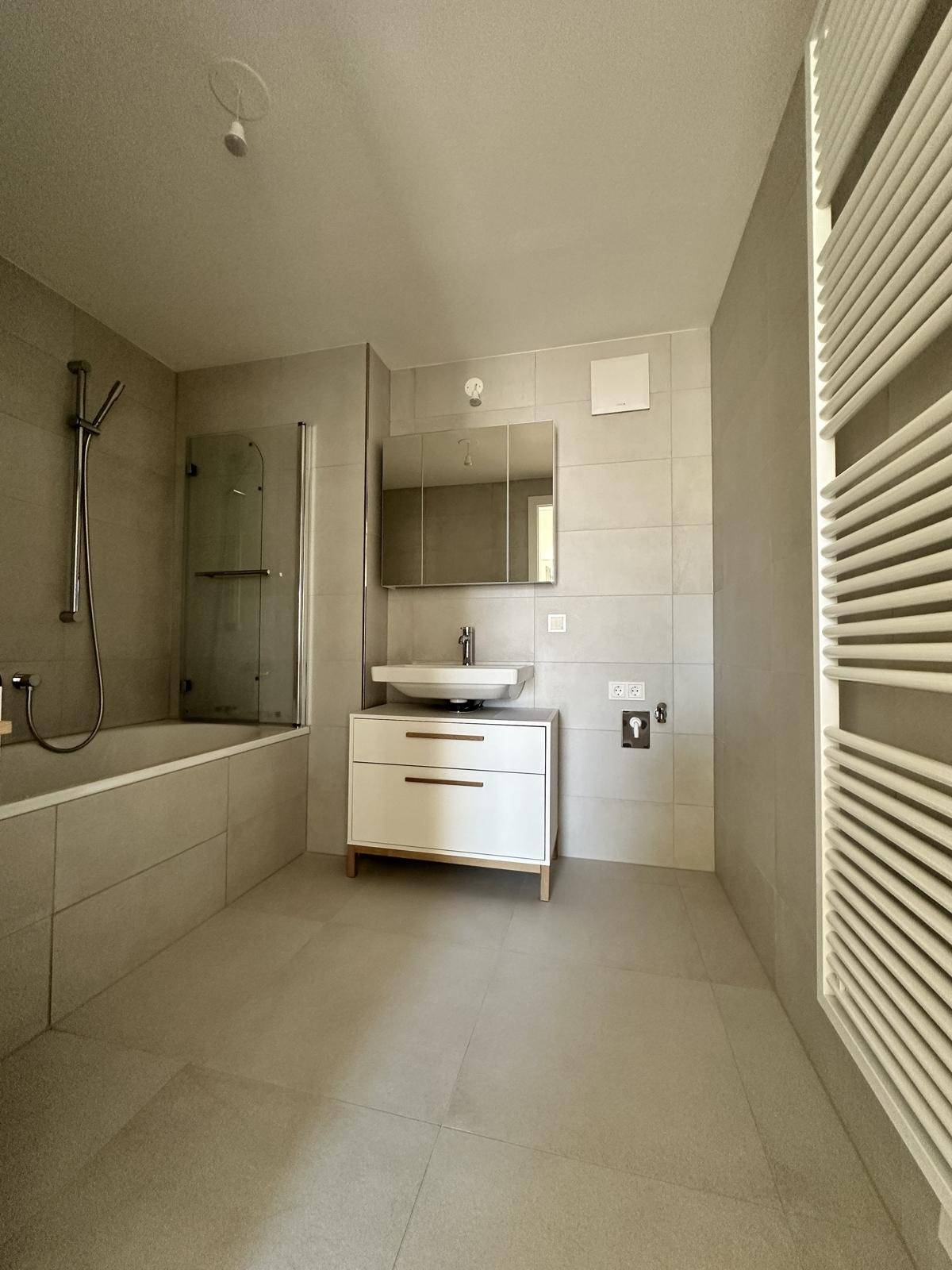 Modernes Badezimmer mit Badewanne, Waschtisch und beheiztem Handtuchhalter, hell gefliest.