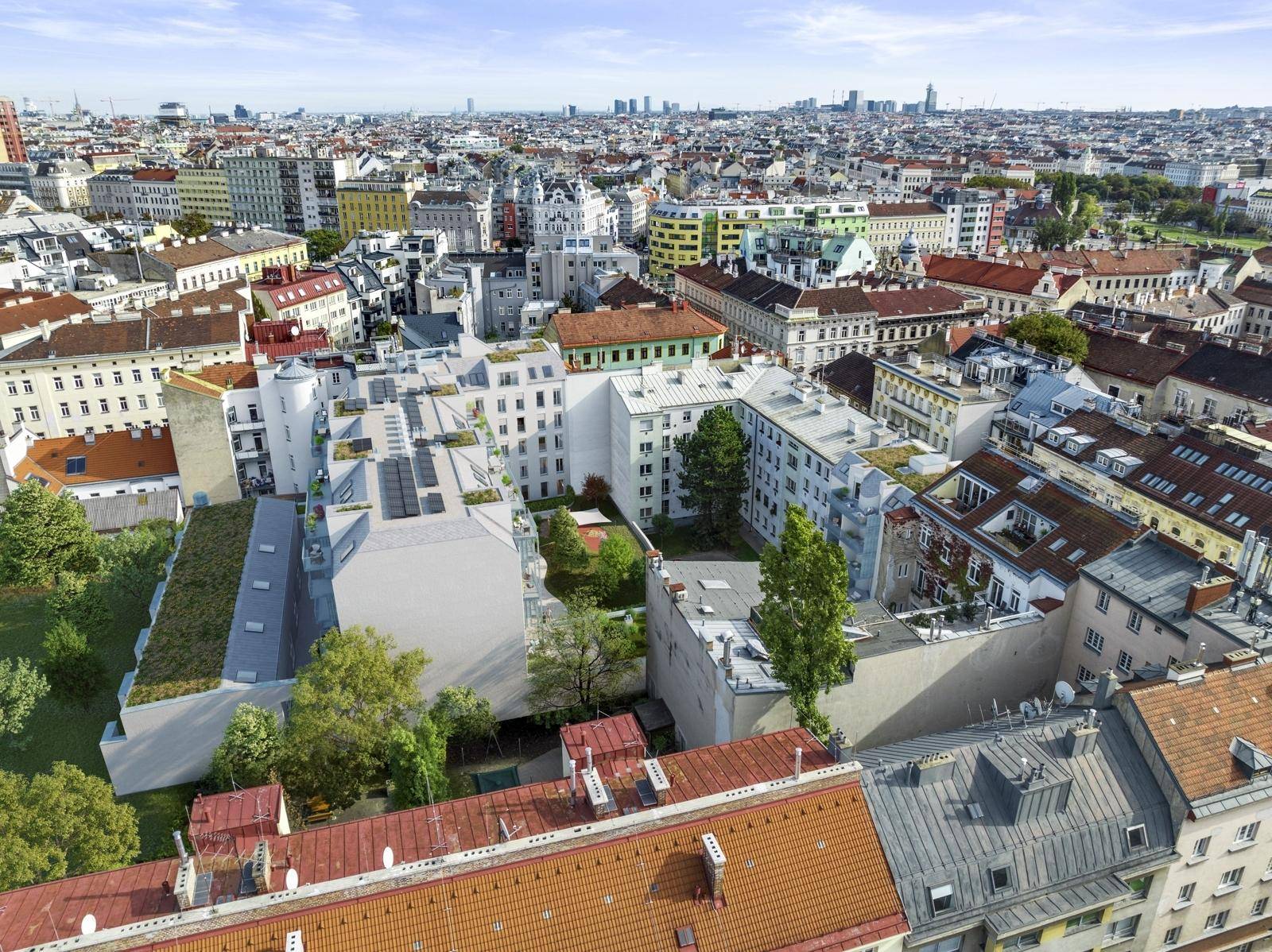 Luftaufnahme einer städtischen Wohngegend mit vielen Gebäuden, grünen Innenhöfen und Dächern unter blauem Himmel.