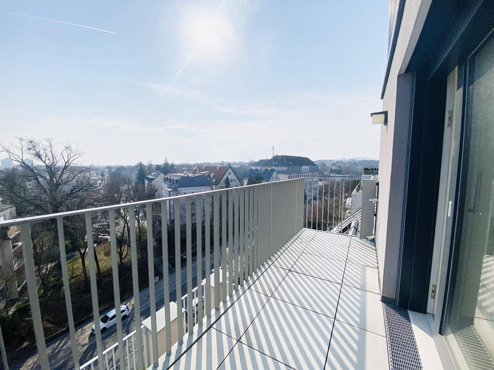 Sonniger Balkon mit Fliesenboden und Blick auf die Stadt und umliegende Gebäude.