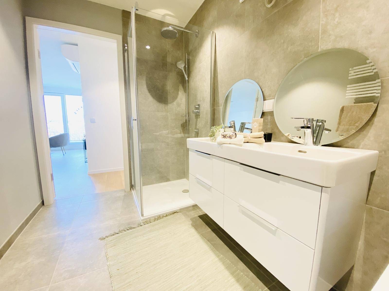 Modernes Badezimmer mit begehbarer Dusche, Doppelwaschbecken und großen Fliesen für ein luxuriöses Gefühl.