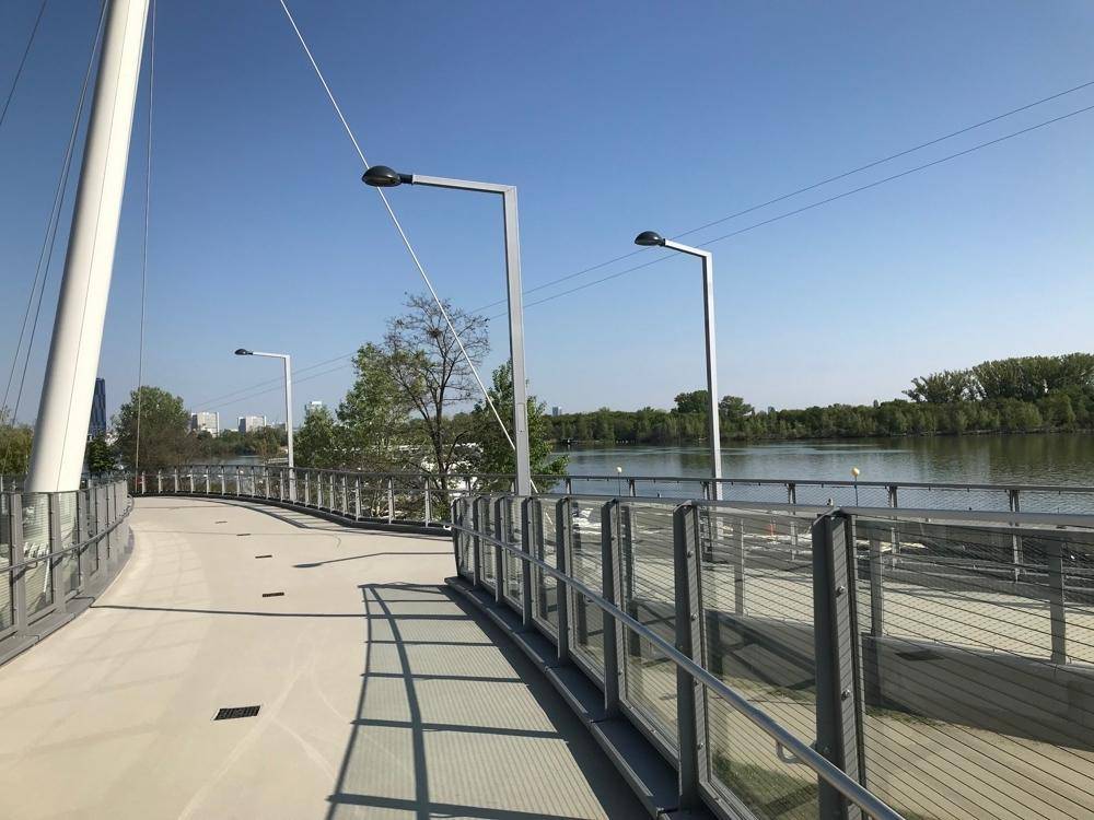 Moderner Fußgängerweg entlang des Wassers mit Brücke und Grünflächen.
