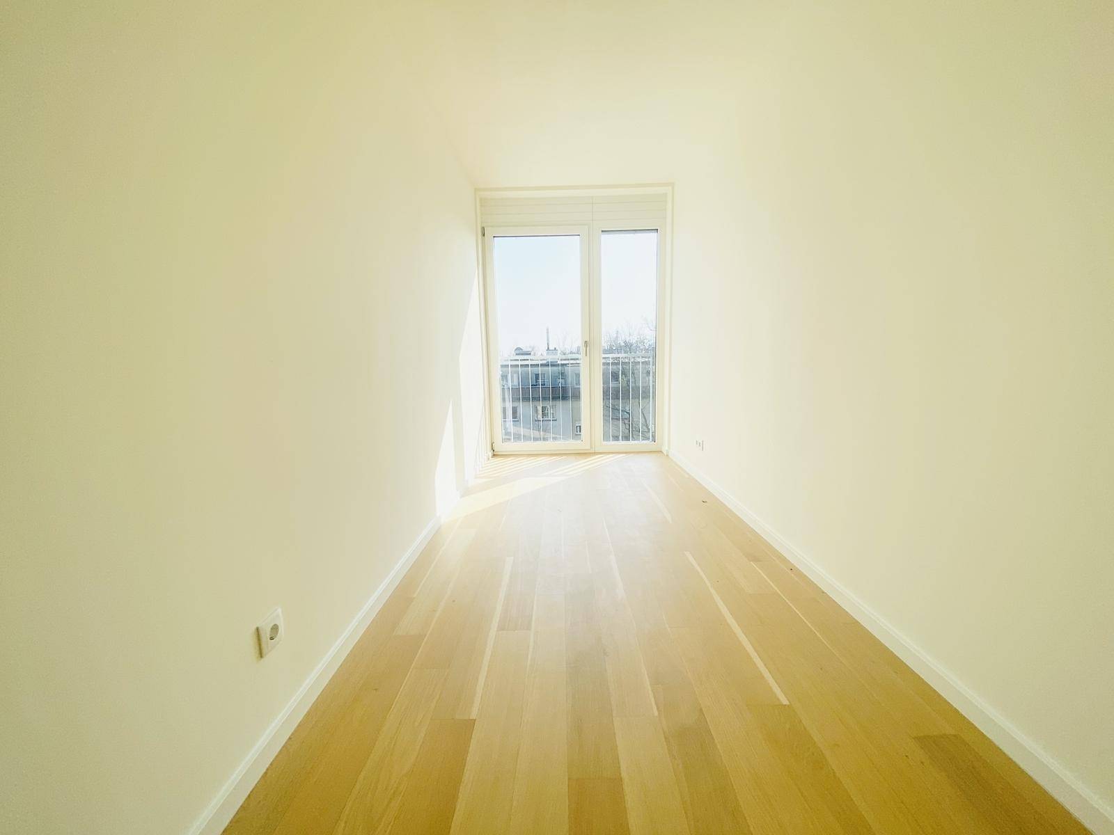 Lichtdurchflutetes Zimmer mit Holzboden und Fenster mit Blick ins Grüne.
