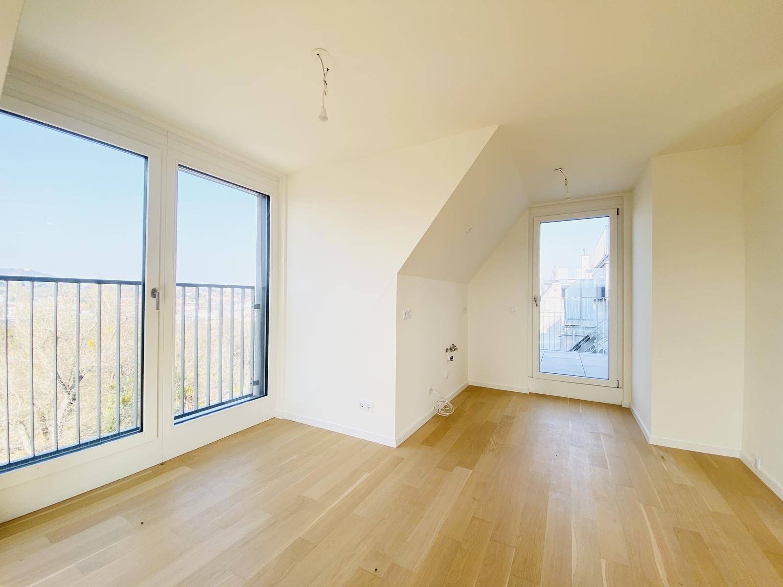 Geräumiges Zimmer im Dachgeschoss mit Holzboden, schrägen Wänden und Zugang zu Außenbereichen.