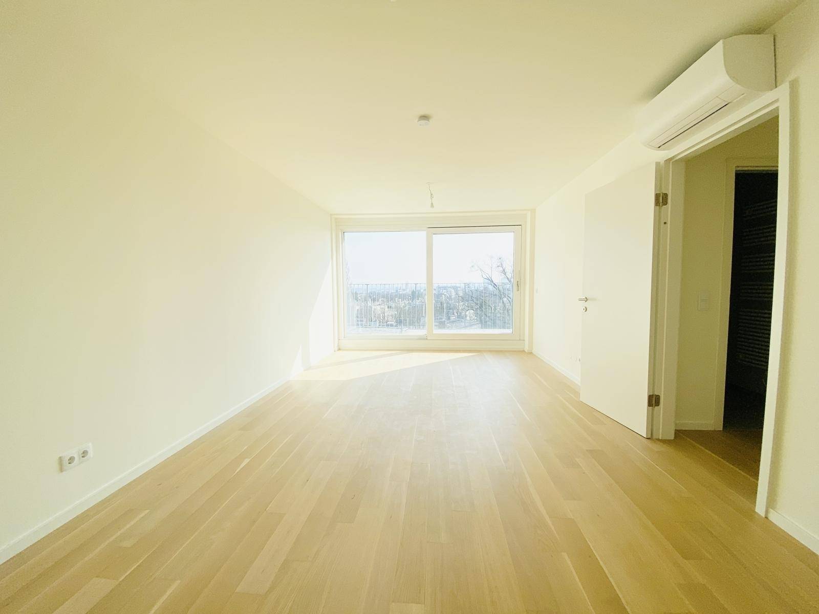 Helles Schlafzimmer mit großen Fenstern, Holzparkettboden und Klimaanlage, bereit zur Einrichtung.