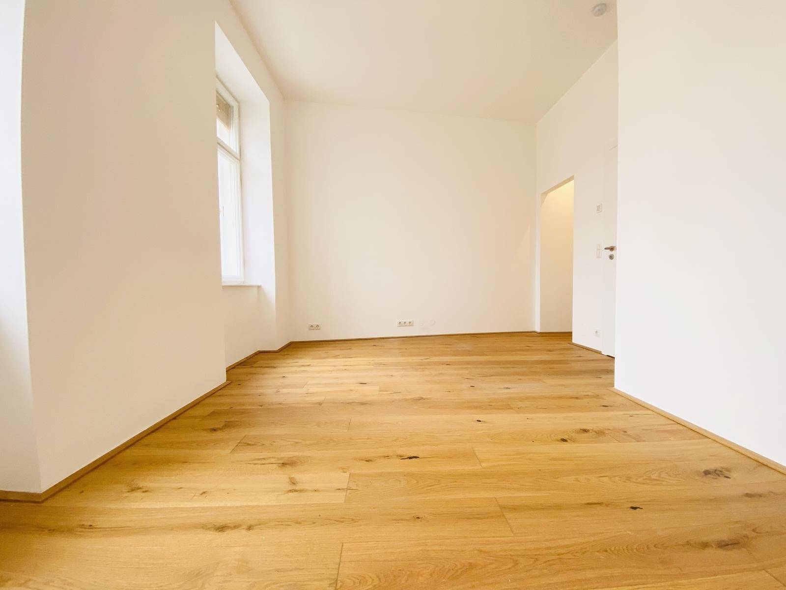 Geräumiges Zimmer mit Holzboden und weiß gestrichenen Wänden, bereit zur Einrichtung.