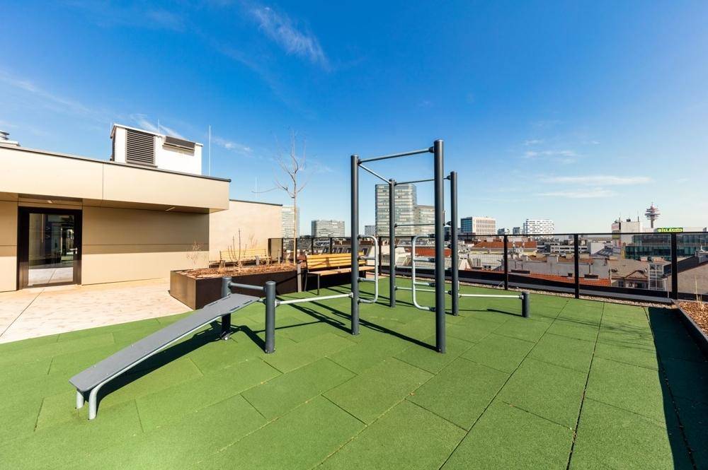 Outdoor-Fitnessbereich auf dem Dach mit verschiedenen Geräten und Panoramablick auf die Stadt.