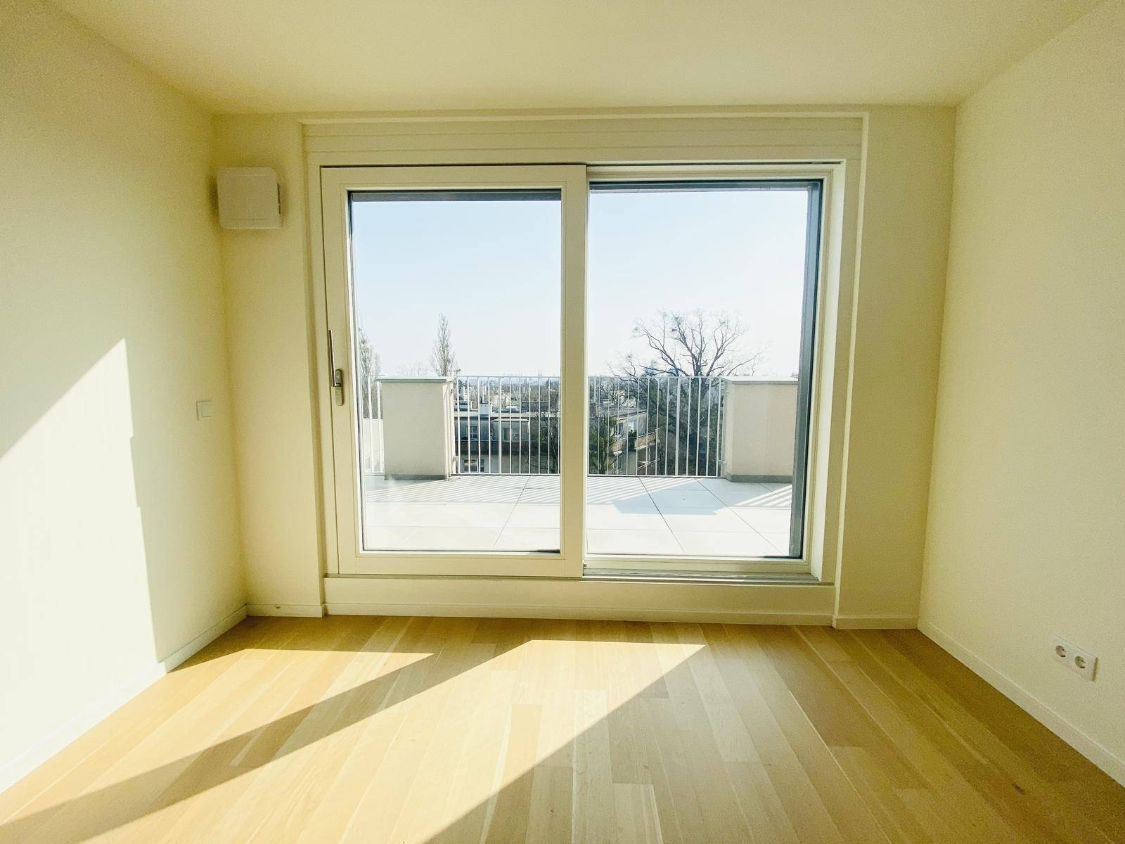 Helles Zimmer mit Parkettboden und großem Fenster mit Zugang zur Terrasse.
