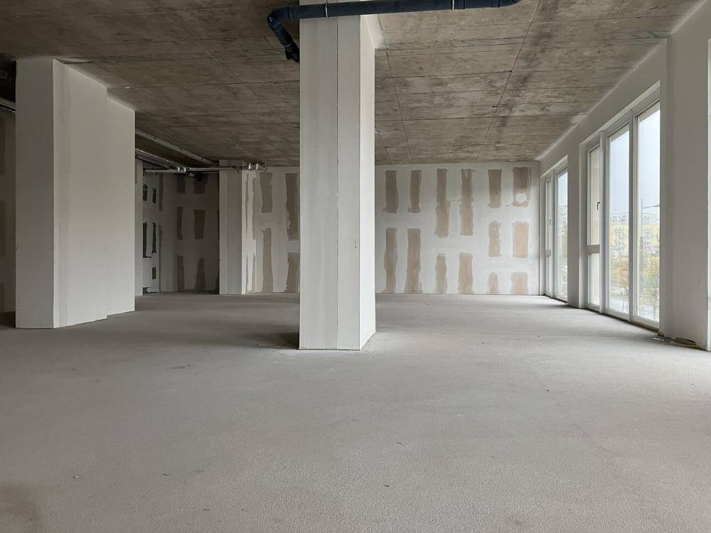 Weitläufiger Rohbau mit Betonboden und hohen Decken, bereit für den Innenausbau und große Fenster.