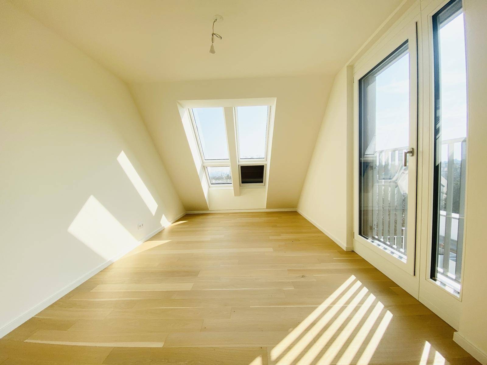 Lichtdurchflutetes Zimmer im Dachgeschoss mit Holzboden, Dachfenster und Zugang zur Terrasse.