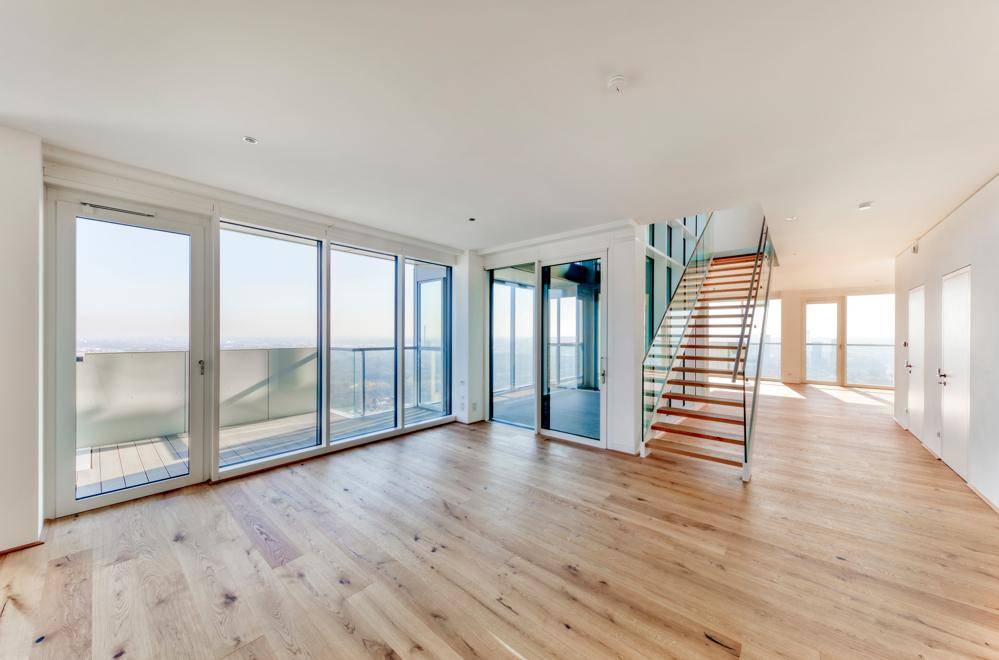 Geräumiger Wohnbereich mit viel Tageslicht, Holzparkett und Zugang zu einem Balkon.