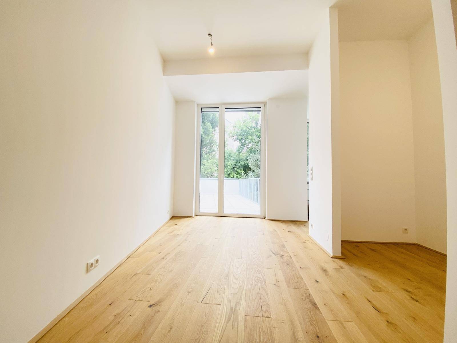 Heller Wohnraum mit Holzboden und großen Fenstertüren, die auf eine Terrasse führen.