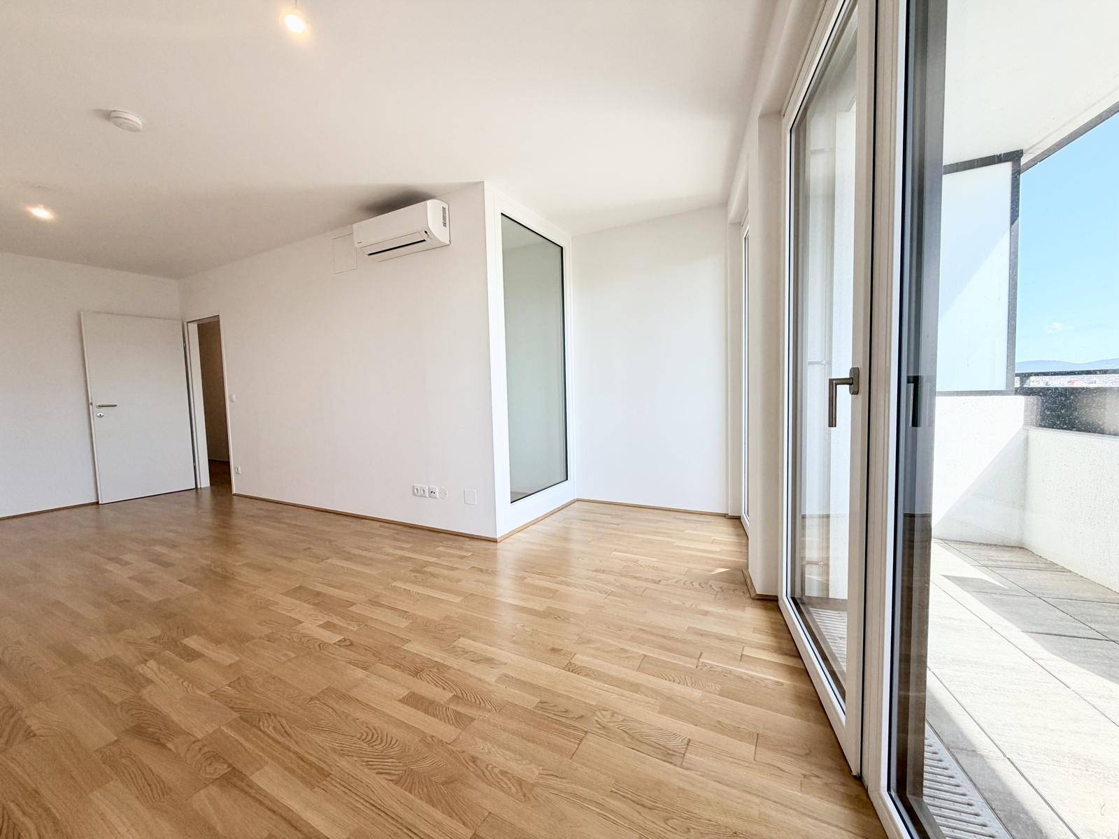 Heller Wohnraum mit Holzboden und Zugang zu einem sonnigen Balkon.