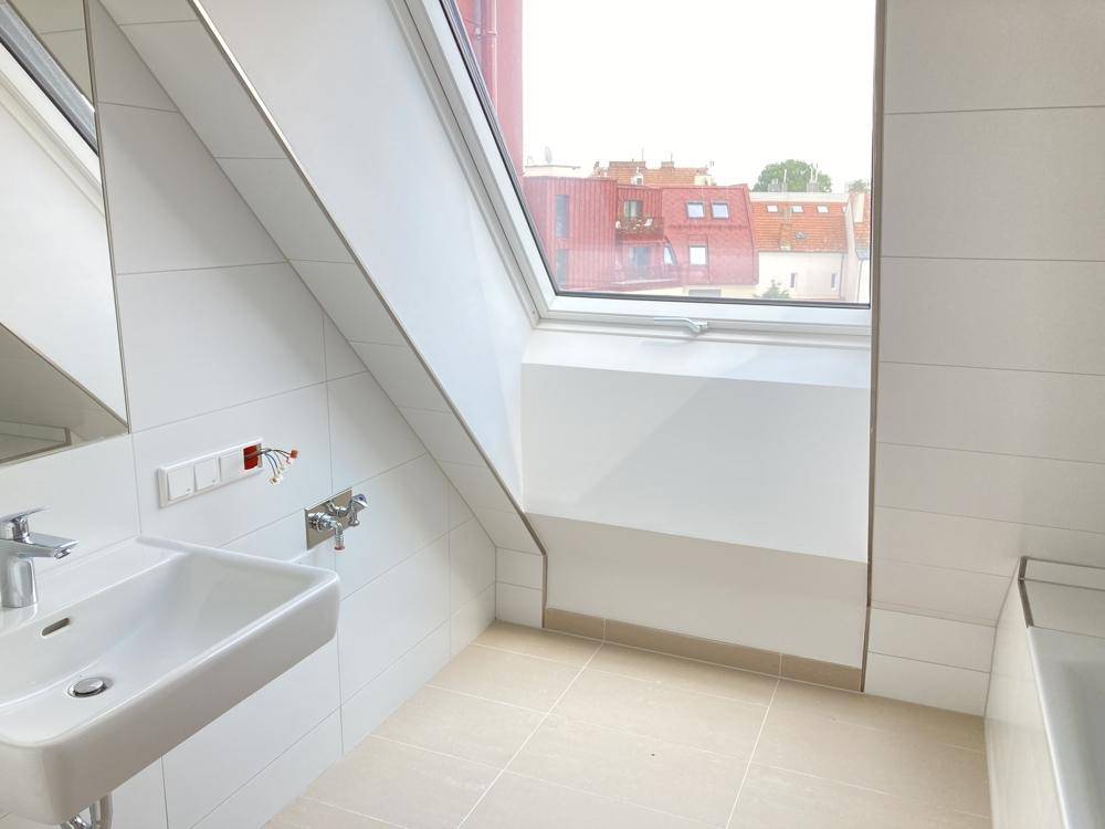 Modernes Badezimmer im Dachgeschoss mit Waschbecken, Badewanne und Dachfenster.