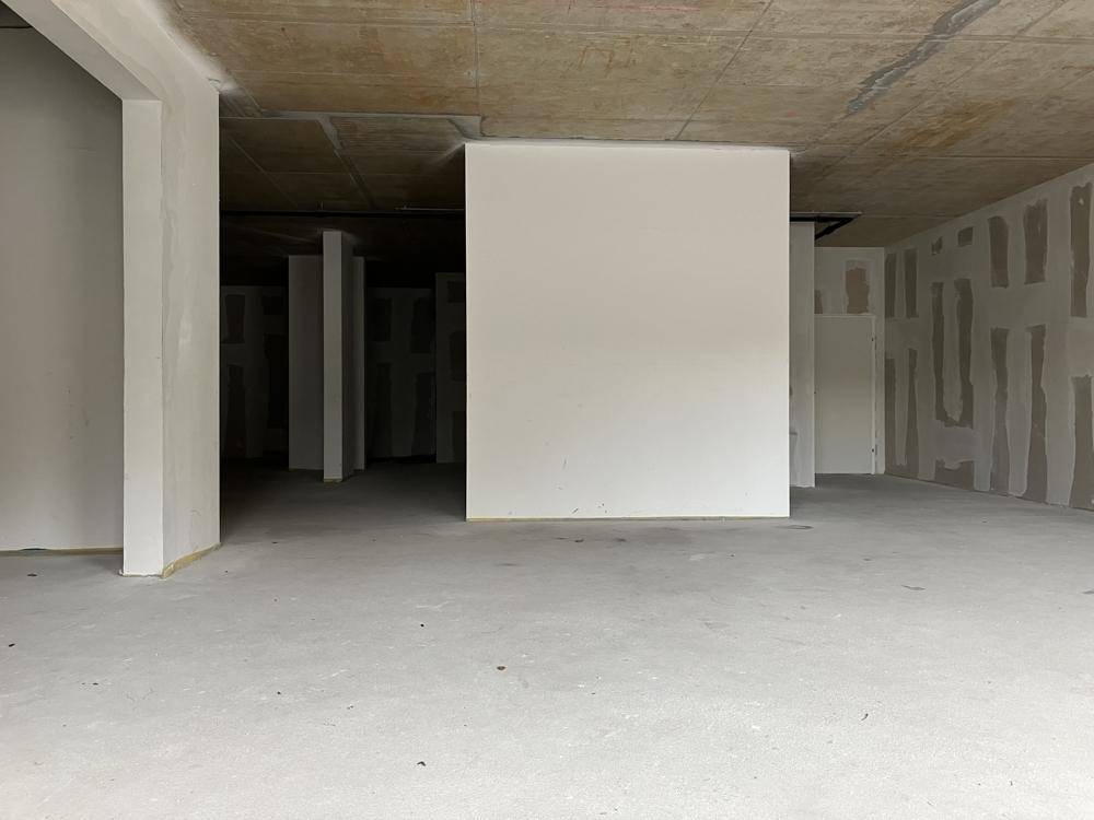 Großer, unfertiger Innenraum mit Betonboden und teilweise verputzten Wänden, ideal für individuelle Gestaltung.