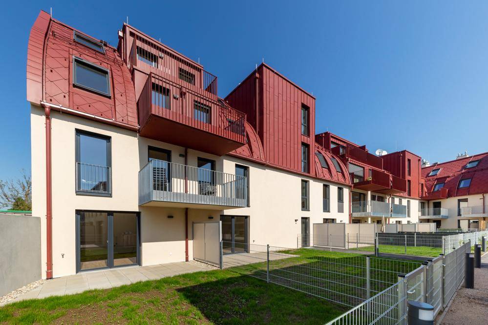 Moderne Wohnanlage mit privaten Gärten und Balkonen unter einem roten Mansarddach.