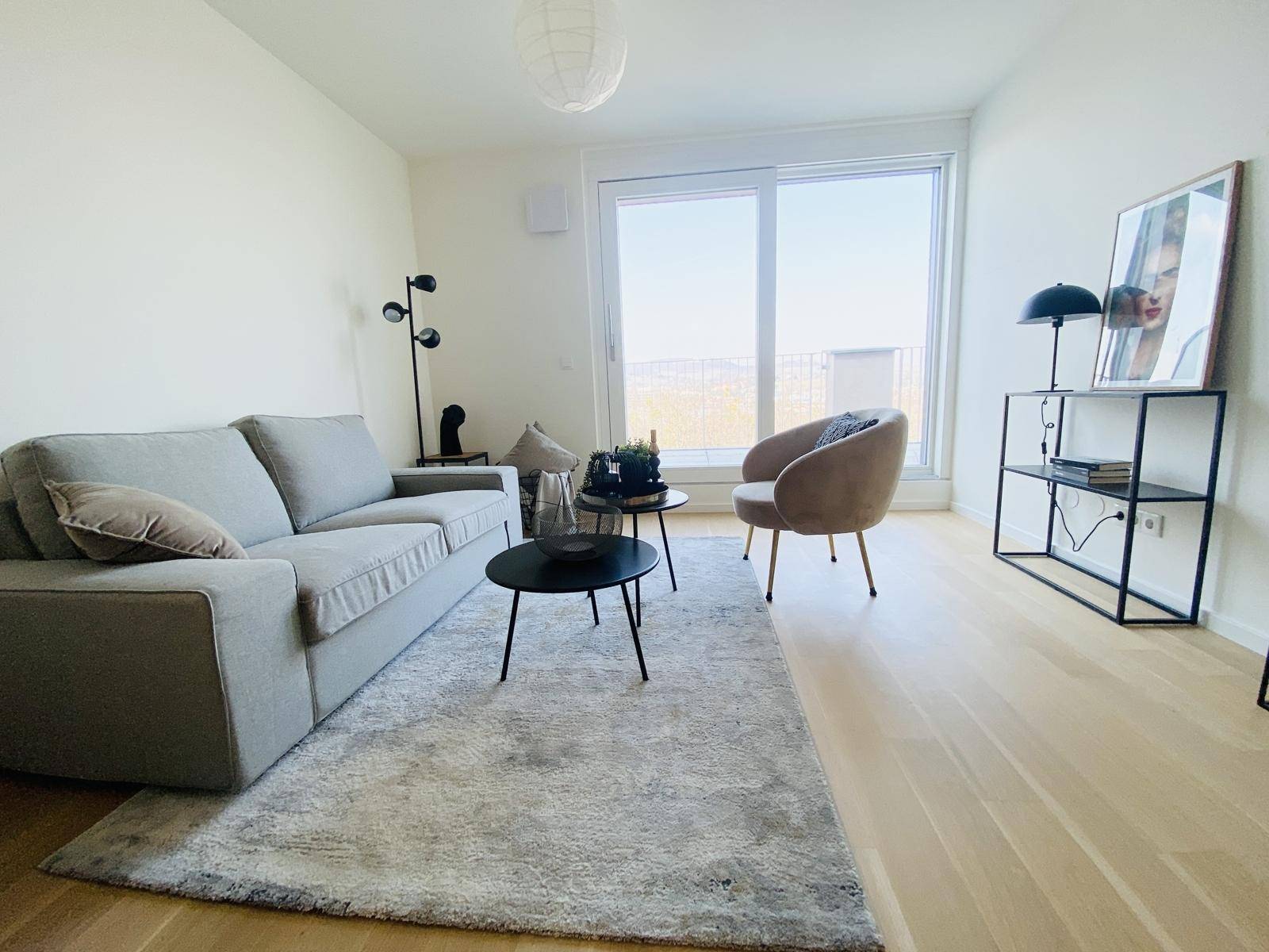 Gemütliches Wohnzimmer mit Sofa, Teppich und großen Fenstern, die einen weiten Blick bieten.