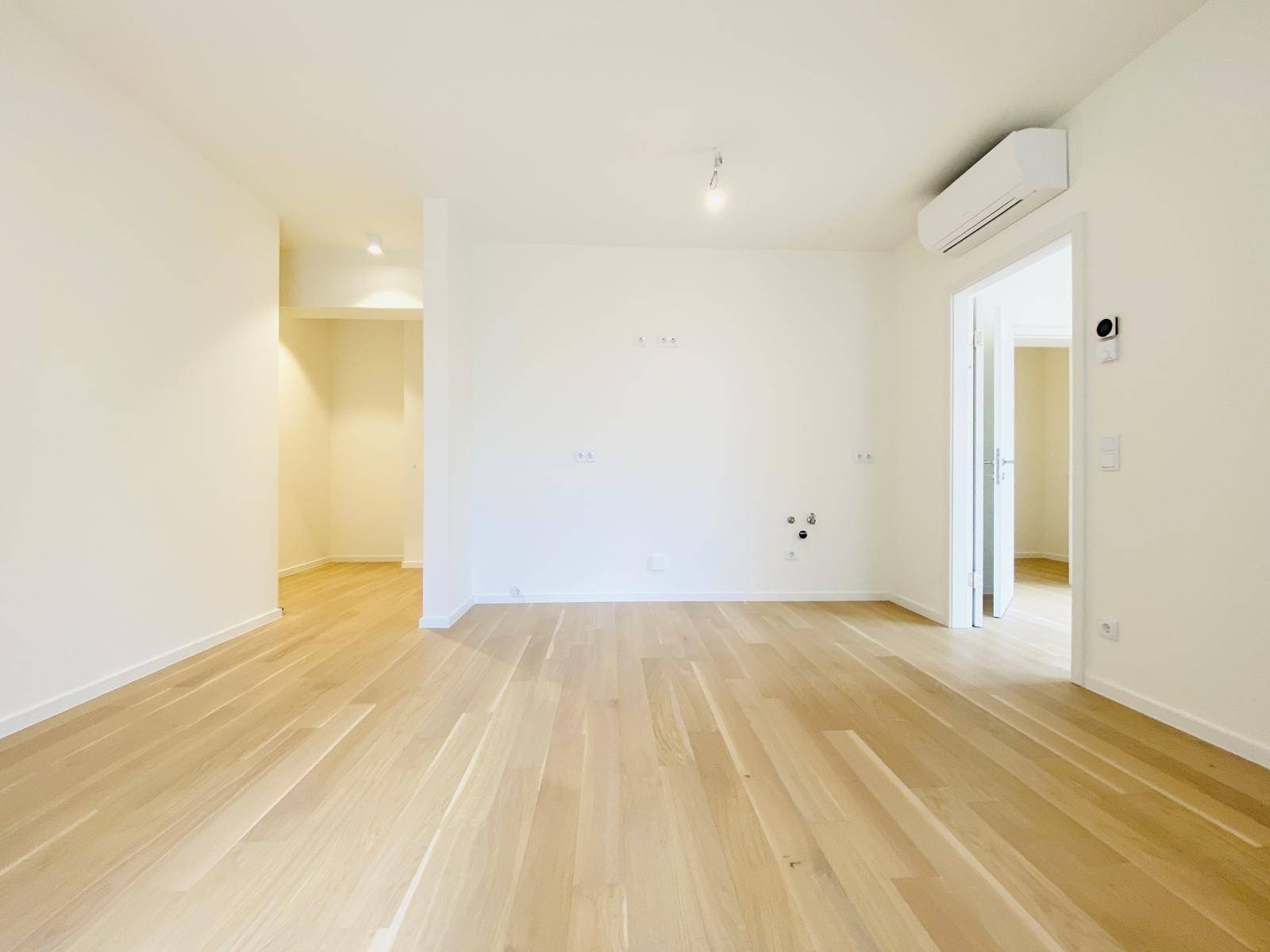 Geräumiges, leeres Zimmer mit Parkettboden, Klimaanlage und Zugang zu weiteren Räumen.