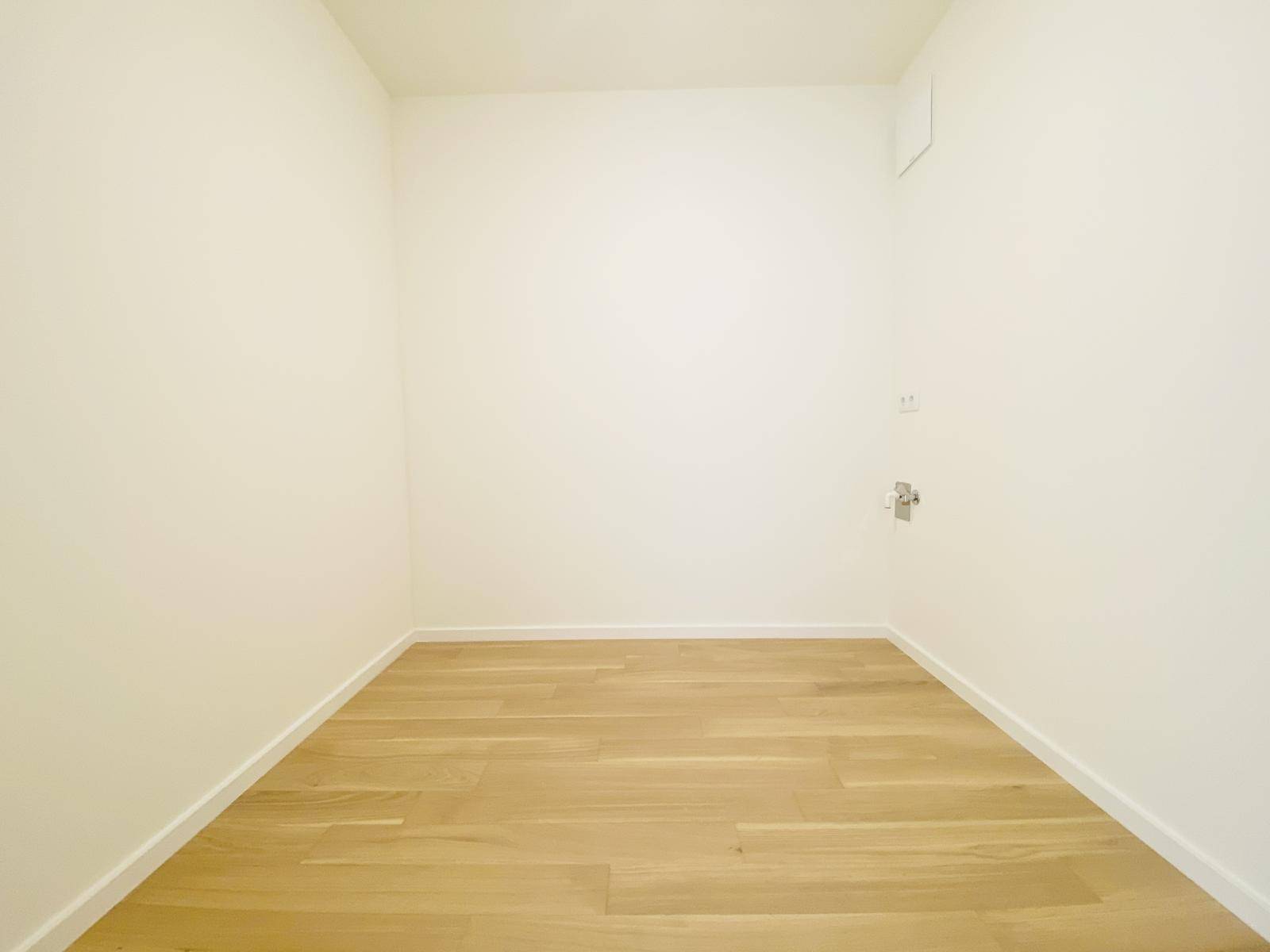 Praktischer Hauswirtschaftsraum mit Holzboden und Anschlüssen für Waschmaschine.
