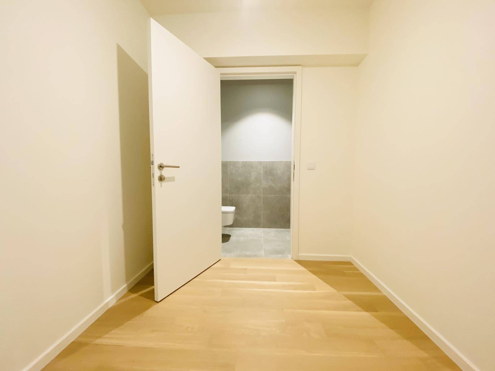 Flur mit hellem Parkettboden und Zugang zu einem modern gefliesten Badezimmer.