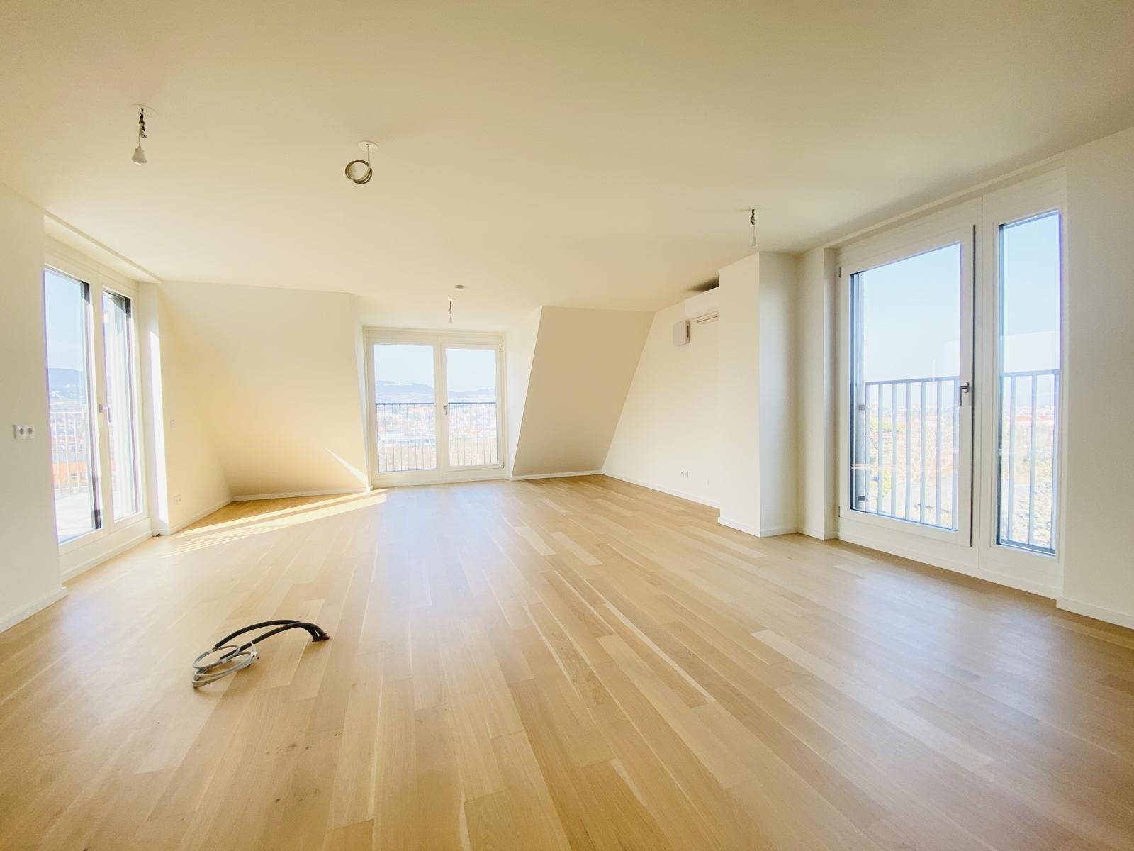 Lichtdurchfluteter Raum mit Holzboden, Dachschräge und Zugang zu einem französischen Balkon.