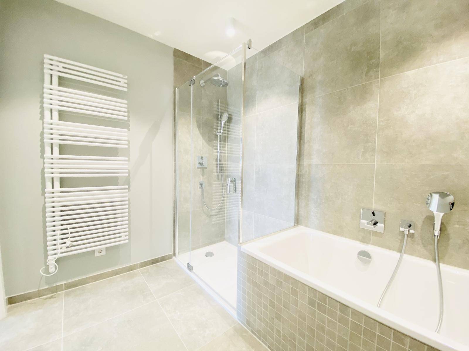 Helles Badezimmer mit Badewanne, Duschkabine und beheiztem Handtuchhalter.