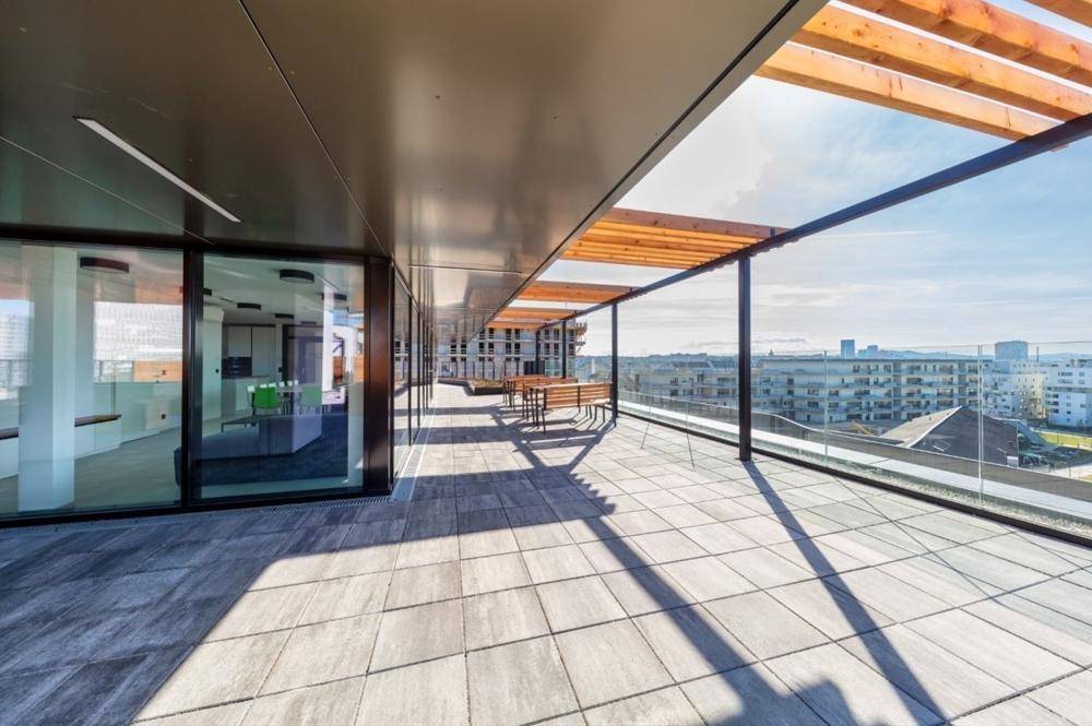 Große, sonnige Dachterrasse mit modernem Fliesenboden, Holzpergola, Sitzbereich und weitem Stadtblick.