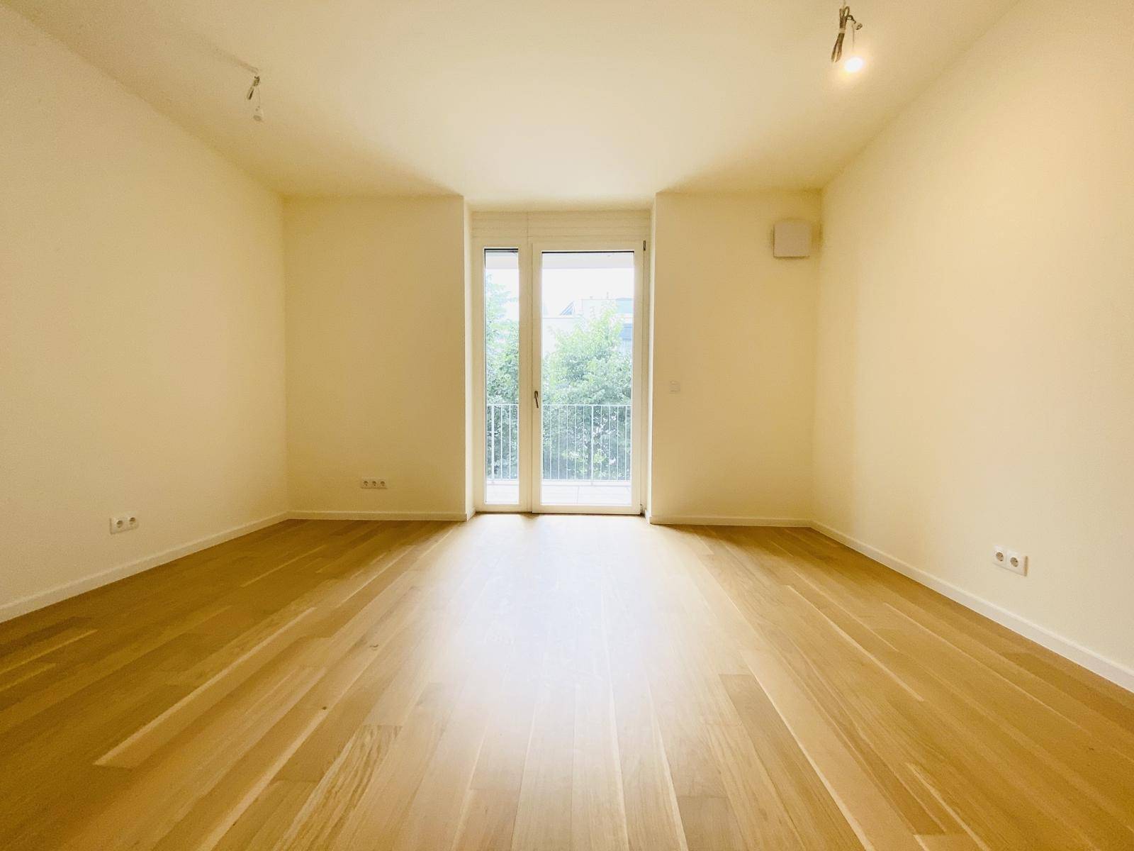 Helles, leeres Zimmer mit Parkettboden und einem Fenster, das einen Blick ins Grüne bietet.