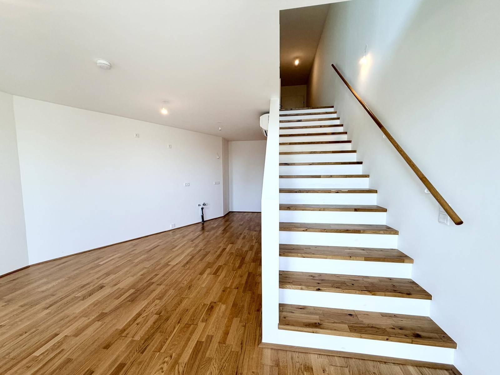 Heller Wohnbereich mit Holzboden und moderner Treppe, die die Ebenen verbindet.