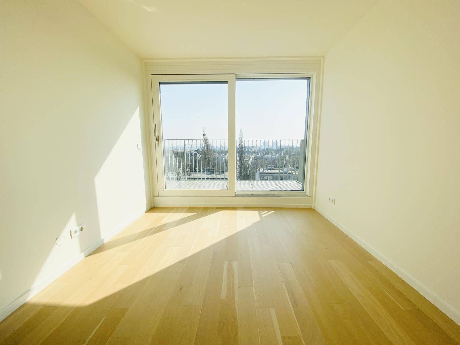 Lichtdurchflutetes Zimmer mit Holzboden und großer Schiebetür zu einem Balkon.