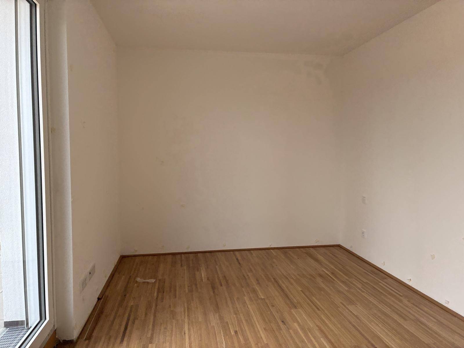 Helles Zimmer mit Holzboden und Zugang zu einem Außenbereich durch eine große Fenstertür.
