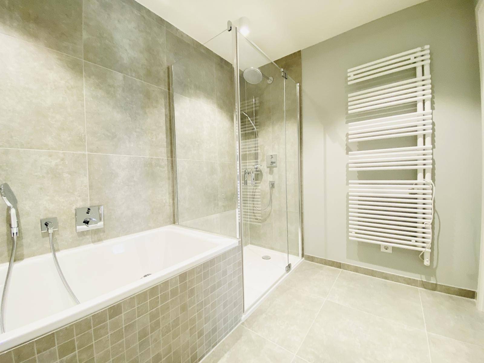 Geräumiges Badezimmer mit Badewanne, Glasdusche und beheiztem Handtuchhalter.