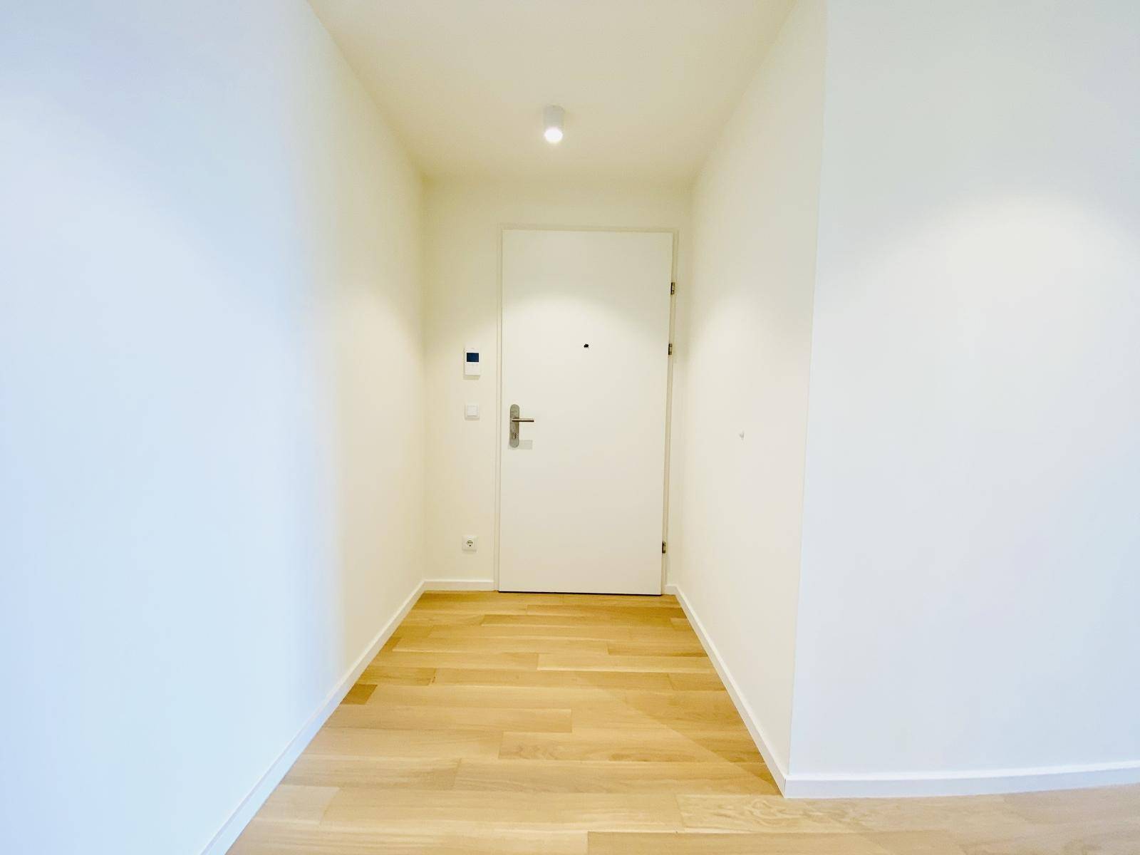 Heller Eingangsbereich mit Holzboden und weißer Tür, der zu den Wohnräumen führt.