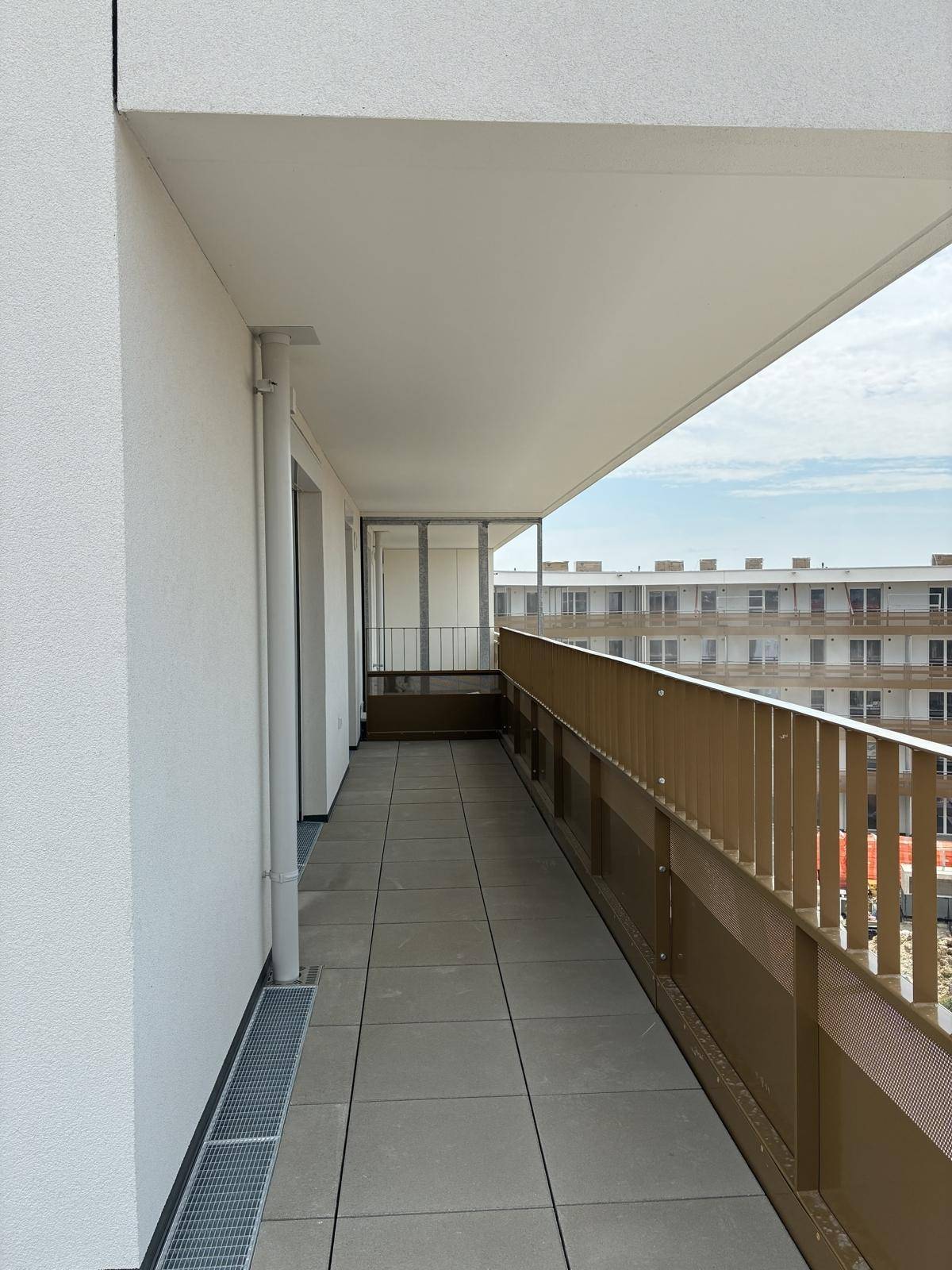 Langer Balkon mit Fliesenboden und Blick auf die umliegenden Gebäude des Neubaukomplexes.