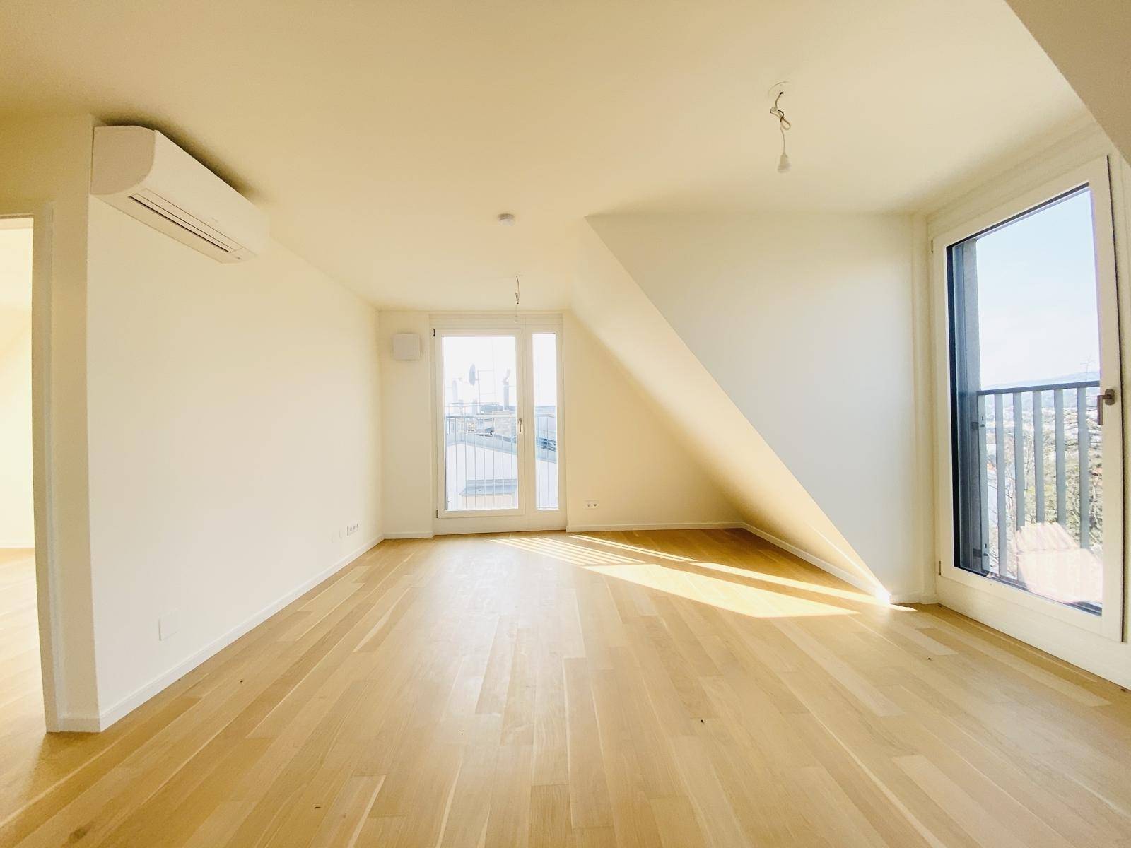 Helles Wohnzimmer im Dachgeschoss mit Holzboden, Klimaanlage und Zugang zu zwei Balkonen.