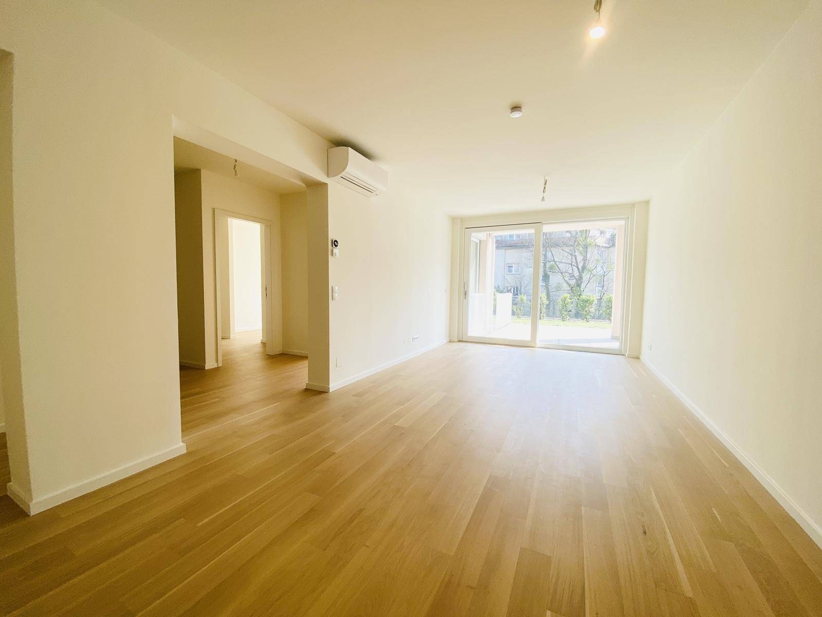 Geräumiges Wohnzimmer mit hellem Parkettboden, großen Schiebetüren und Klimaanlage.