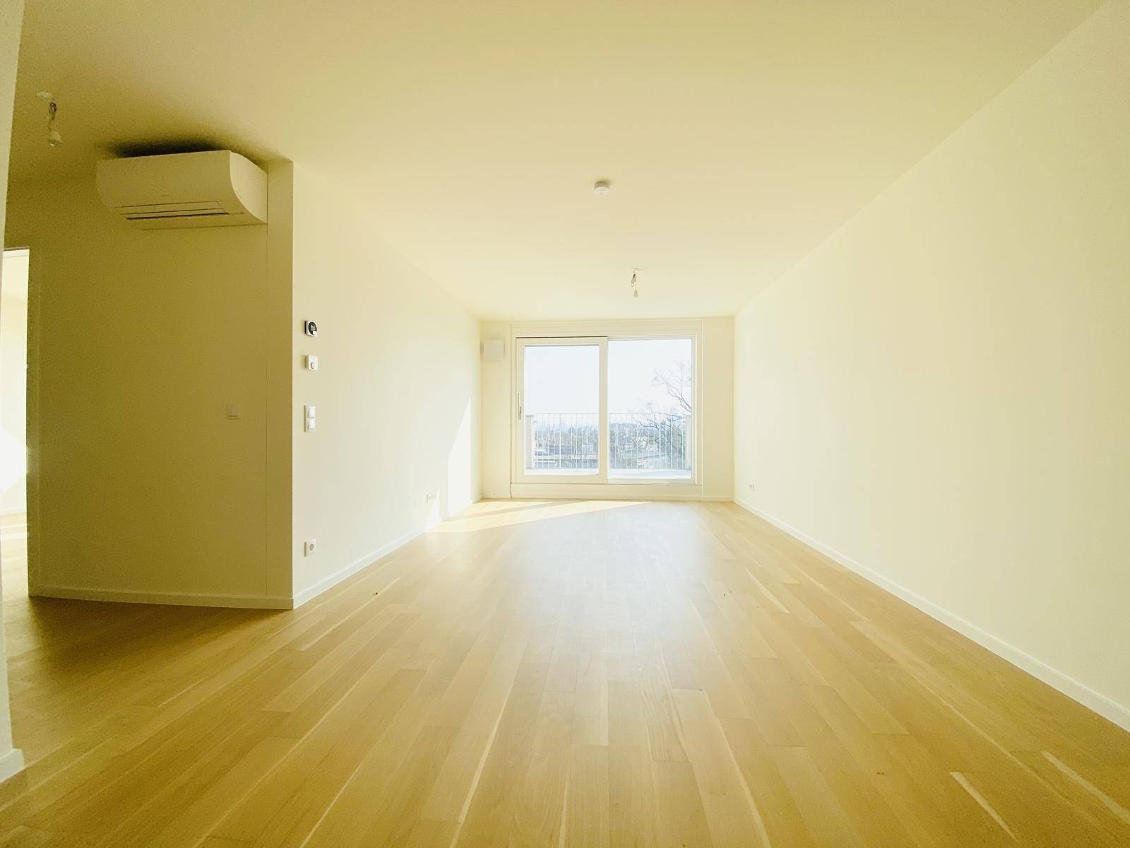 Geräumiges, helles Wohnzimmer mit Parkettboden, Klimaanlage und Zugang zum Balkon.